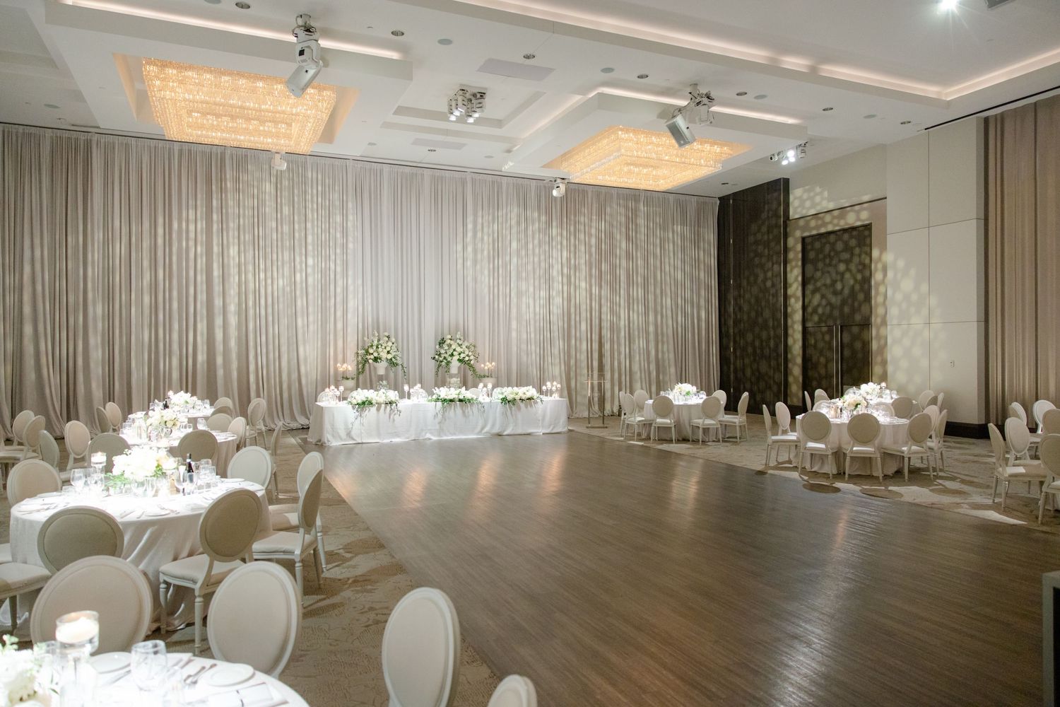 Modern wedding venue with crystal chandeliers, white drapery and round dining tables.