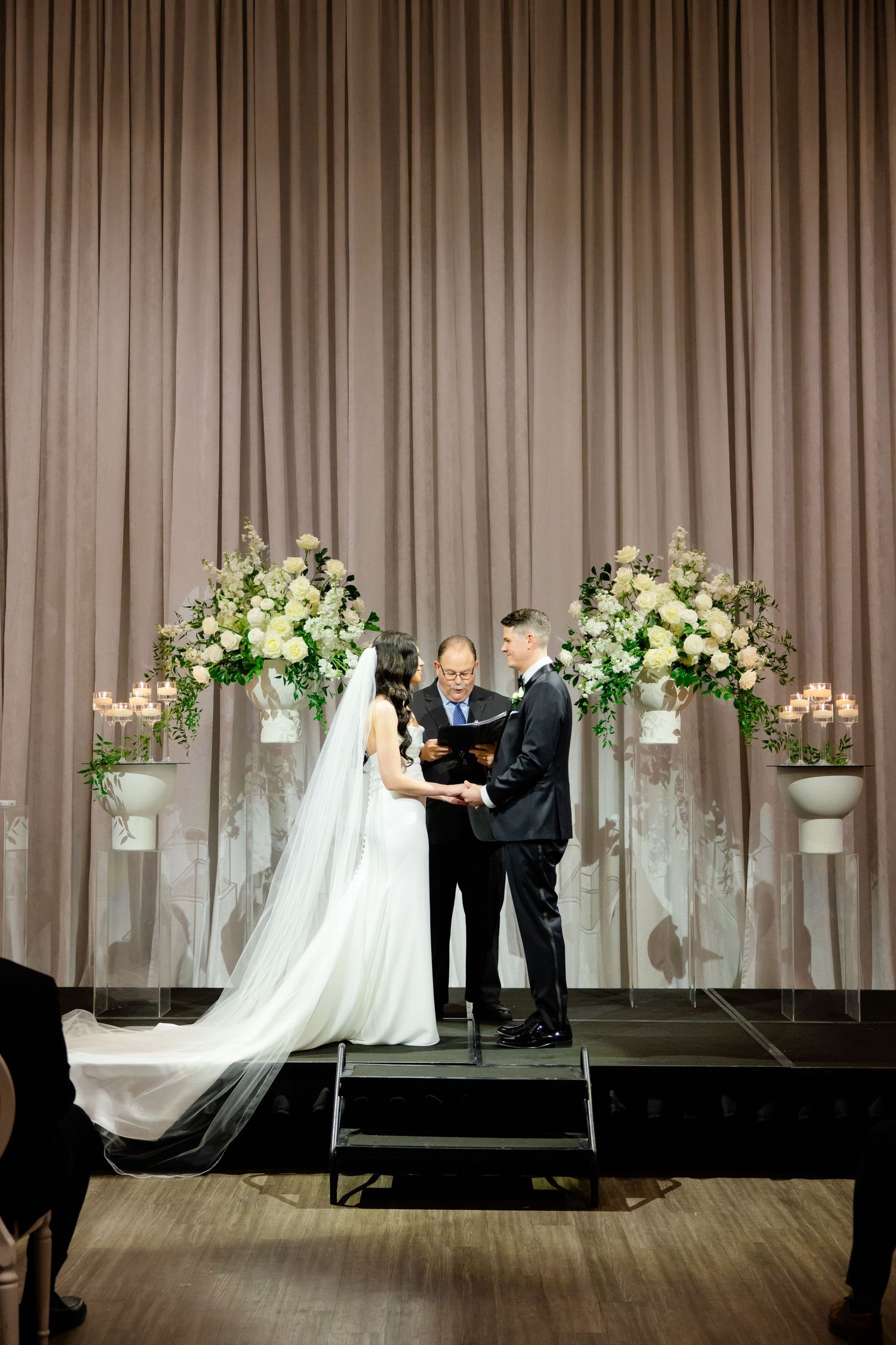 Intimate wedding ceremony on raised platform with romantic candlelight and white floral arrangements.
