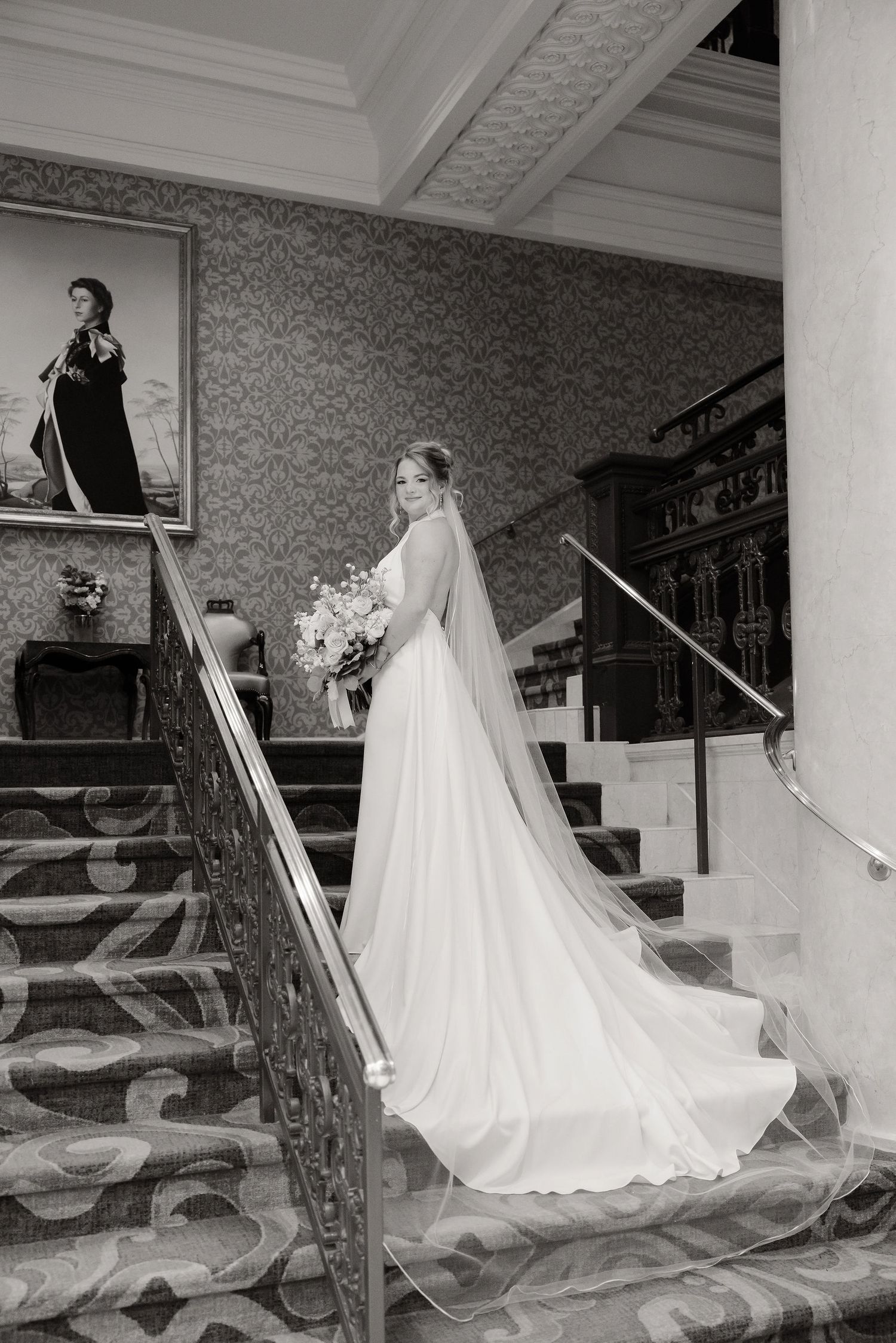 Elegant bridal portrait on a grand staircase with patterned wallpaper and flowing veil.