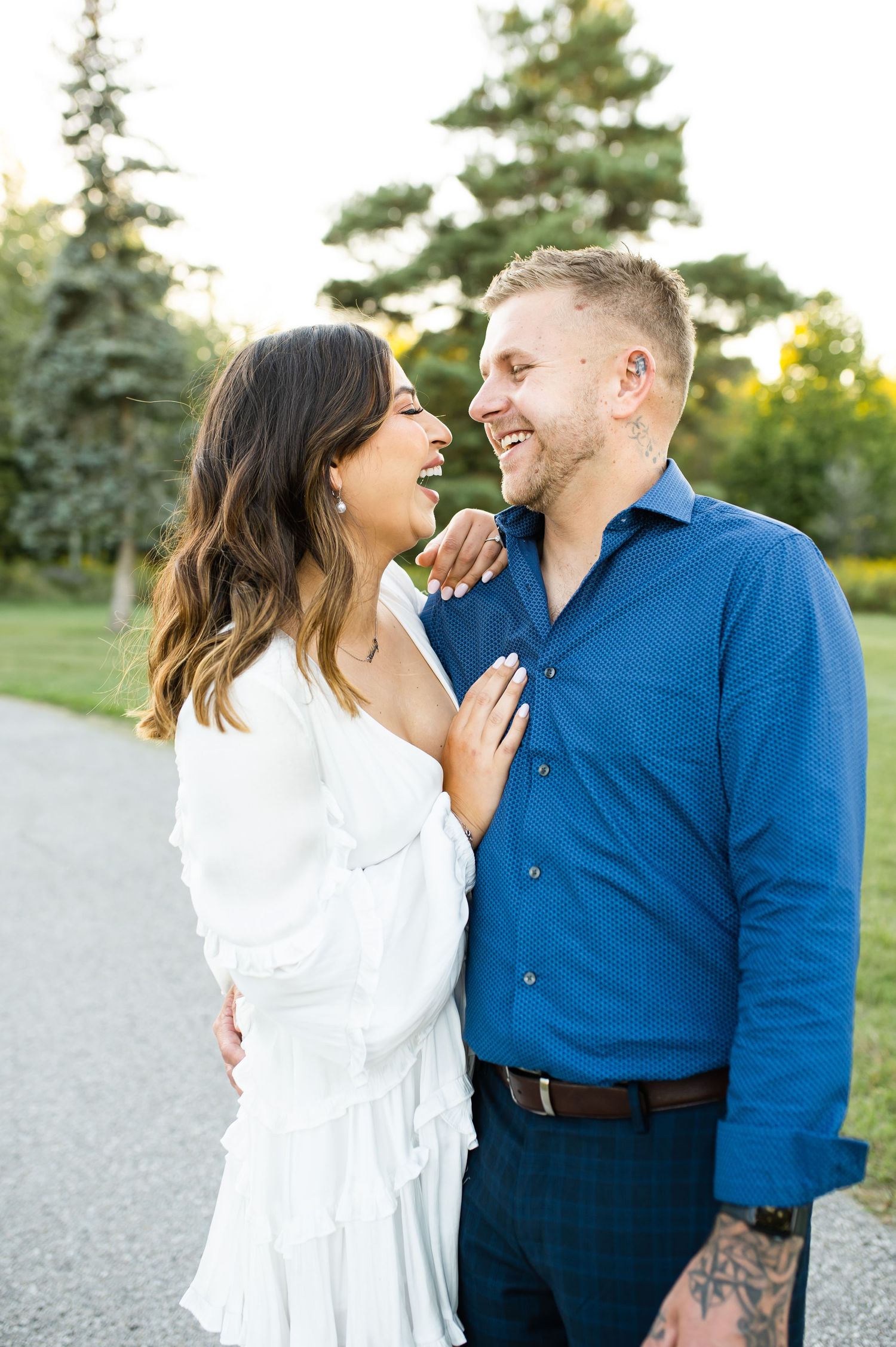 Couple sharing laughter together on path with evergreen trees in background.