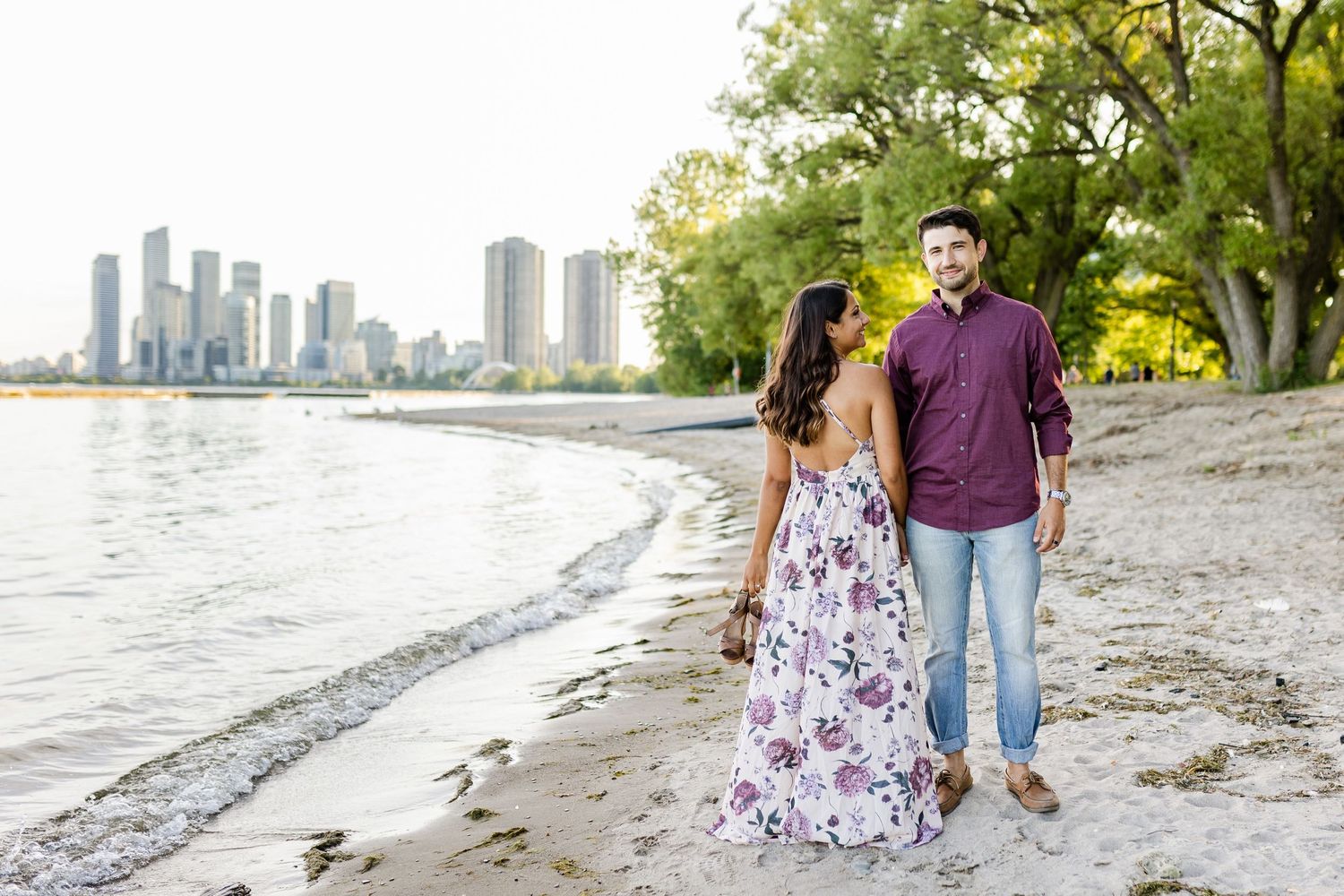 Romantic beachside portrait with cityscape and trees framing the scene.