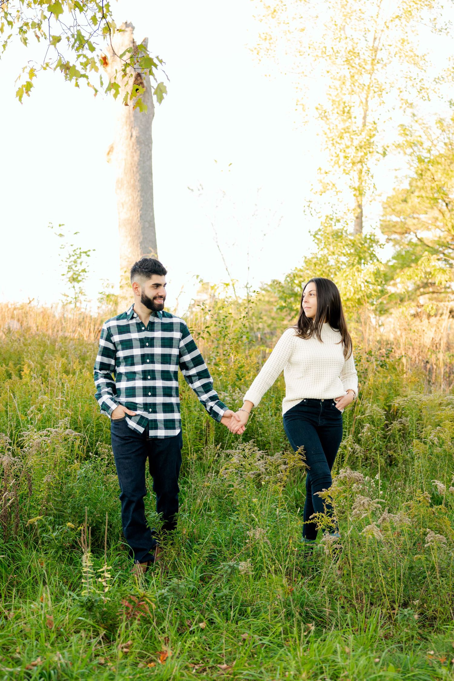 Couple holding hands while walking through tall grass field at sunset.