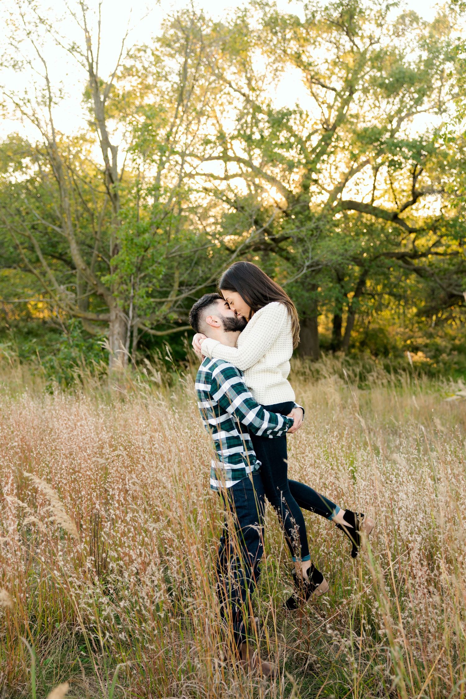 Romantic embrace in tall grass field during golden sunset.