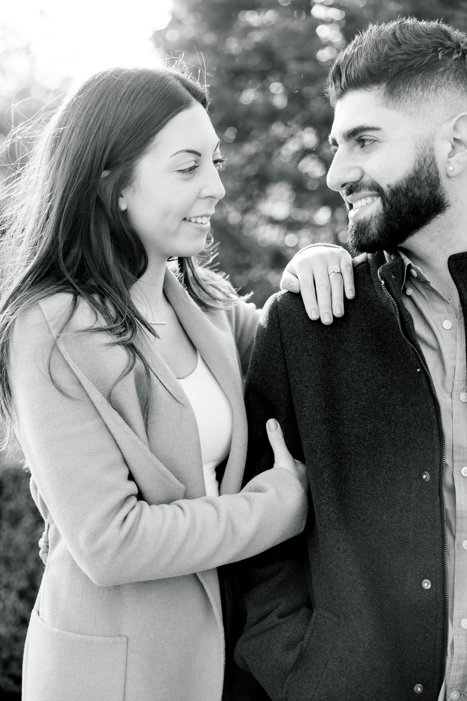 Romantic black and white portrait of couple smiling at each other in a garden setting.