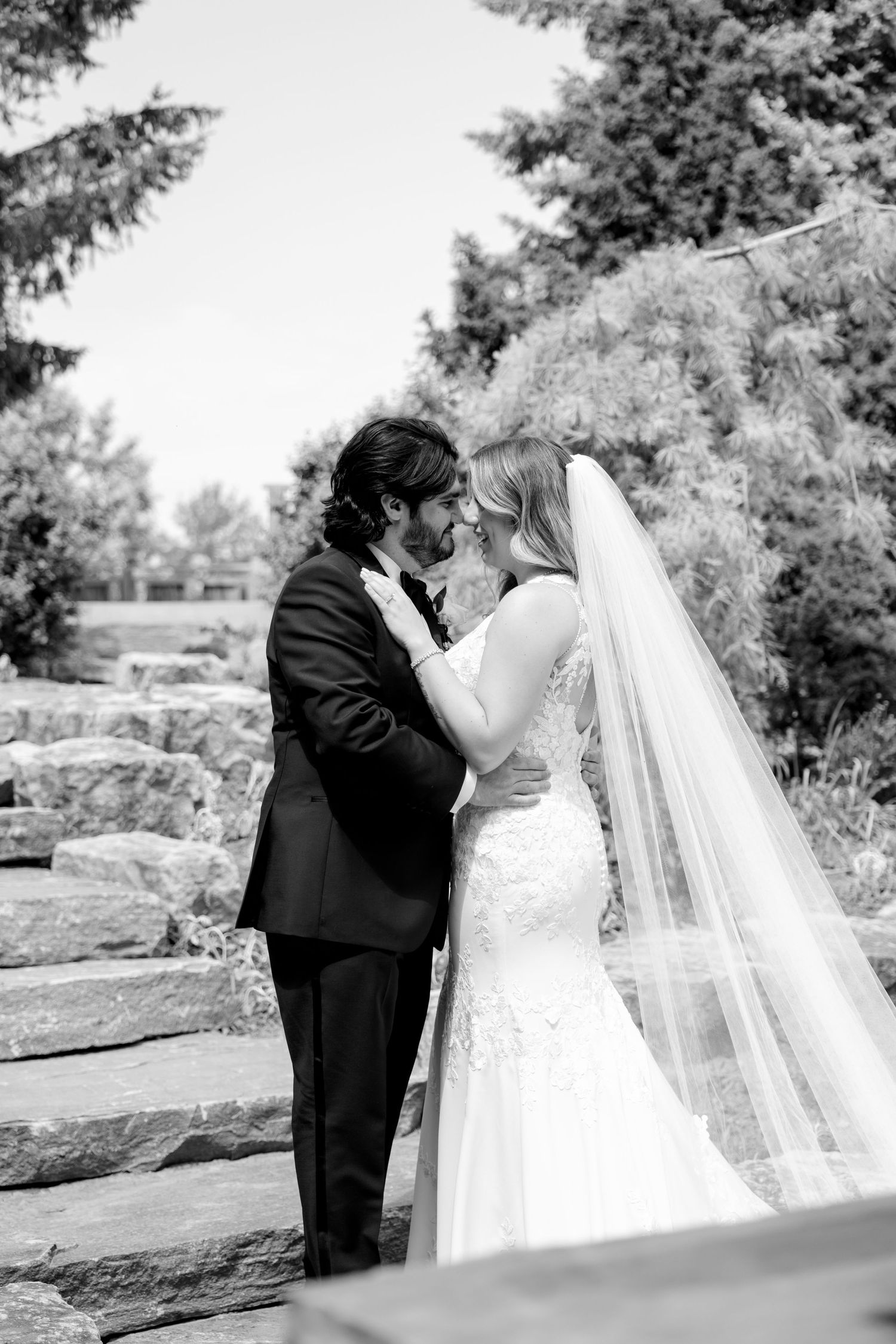 Black and white intimate wedding portrait on stone steps with flowing veil.