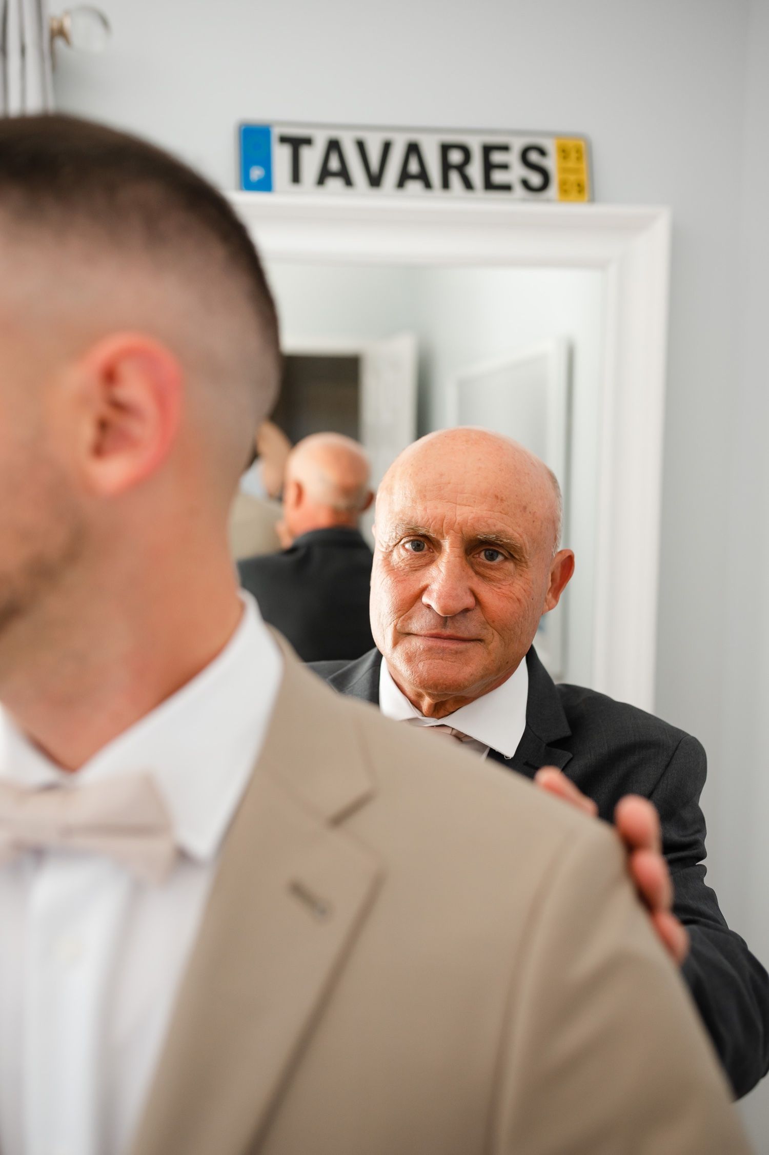 A formal dressing moment captured under a Tavares sign with reflections in the mirror.