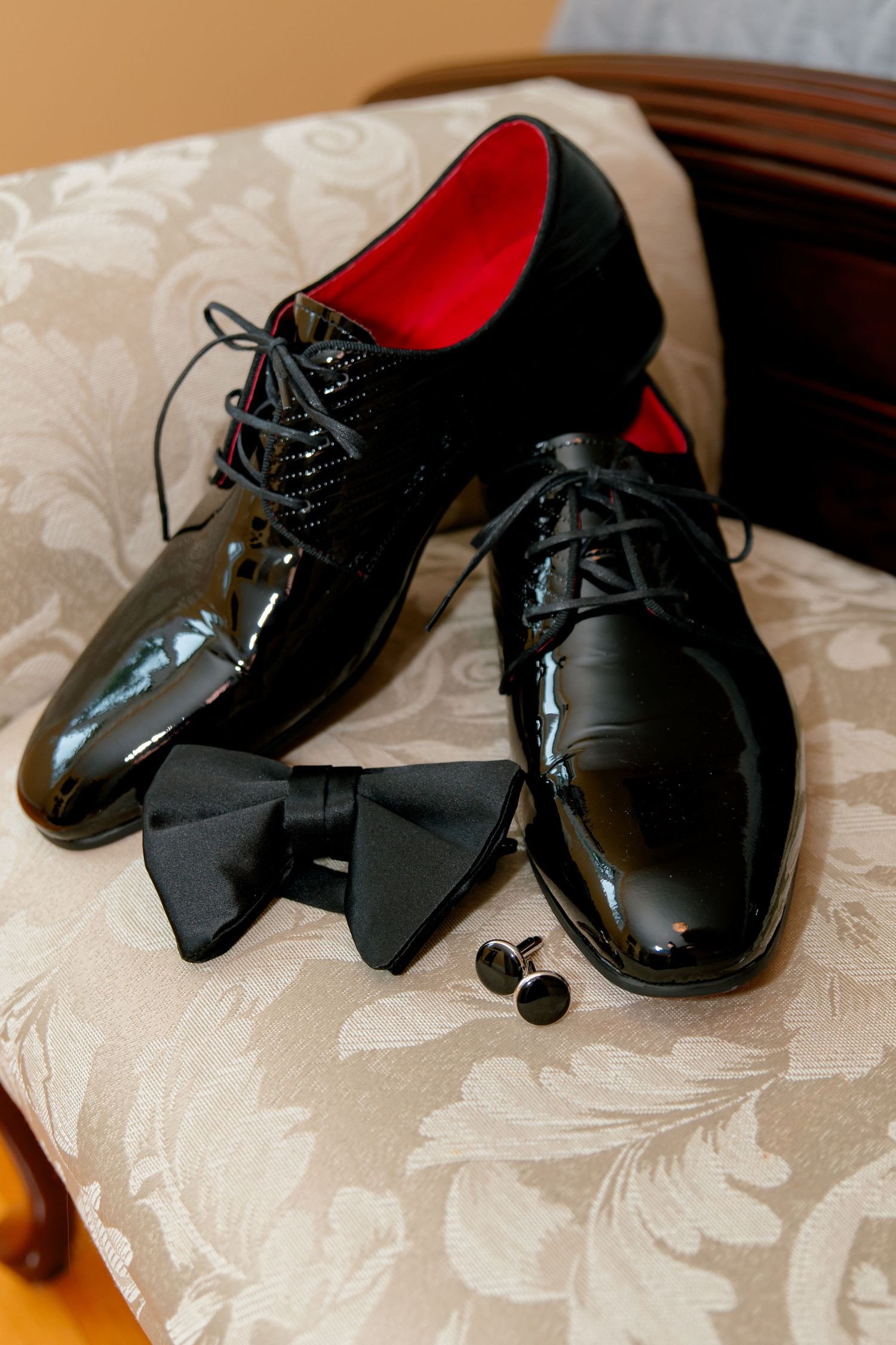 Patent leather dress shoes with black bow tie and cufflinks on textured fabric.