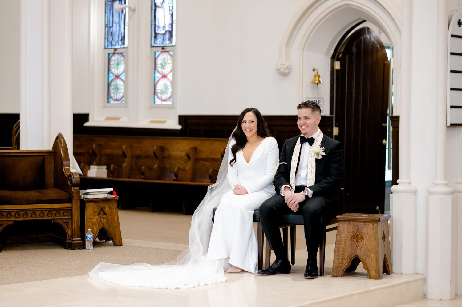 A couple sits together during their traditional wedding ceremony in an elegant church setting.