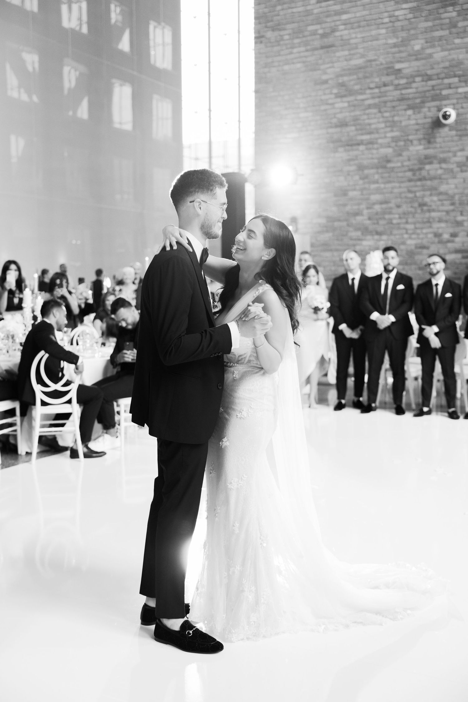 Black and white wedding dance moment in an industrial venue with exposed brick walls.