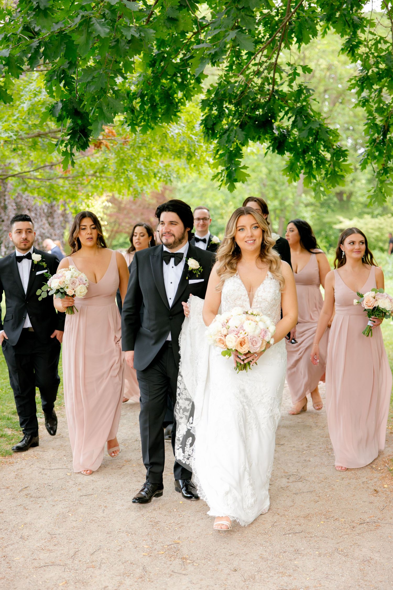 Wedding party walking along garden path with bridesmaids in pink dresses.