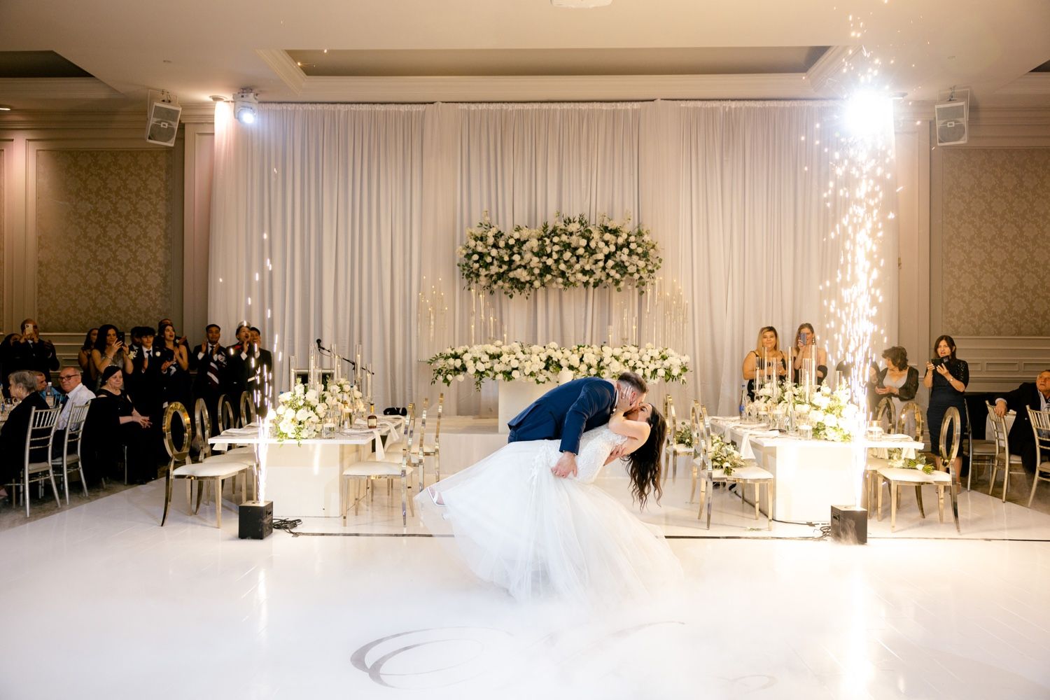 Dramatic dip during first dance at wedding reception with sparklers and elegant white decor.