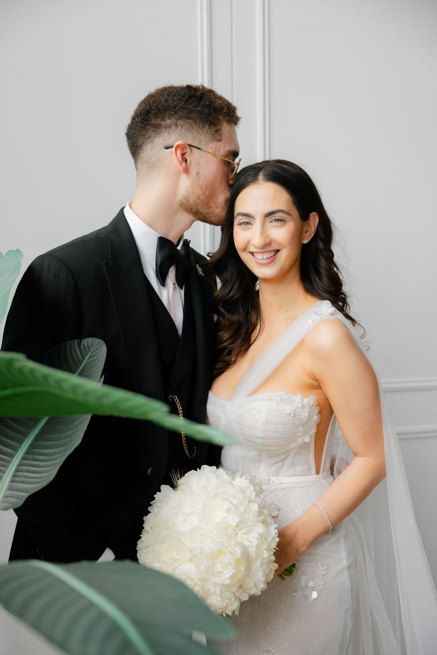 Romantic wedding portrait with tropical leaves framing intimate moment.