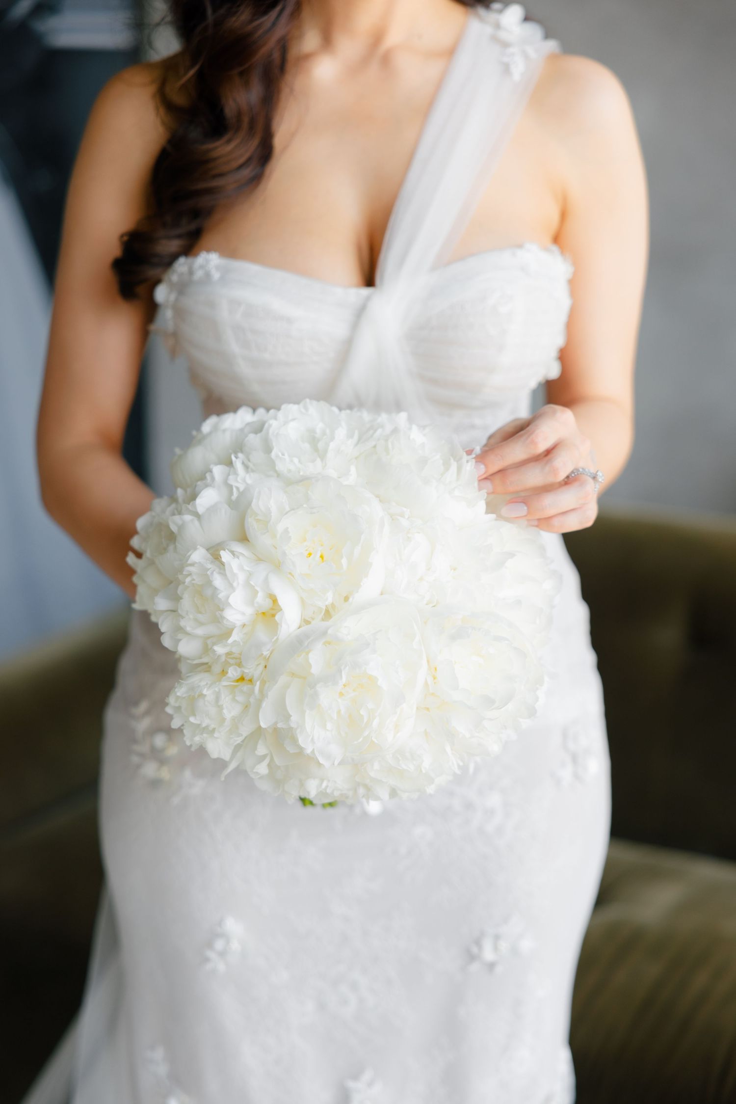 Close-up of white wedding dress details and large peony bouquet.