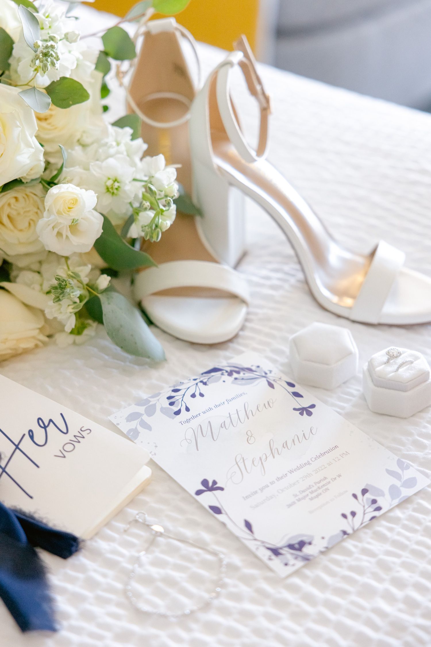 Elegant wedding invitation with white roses and cream heels on textured white linen.