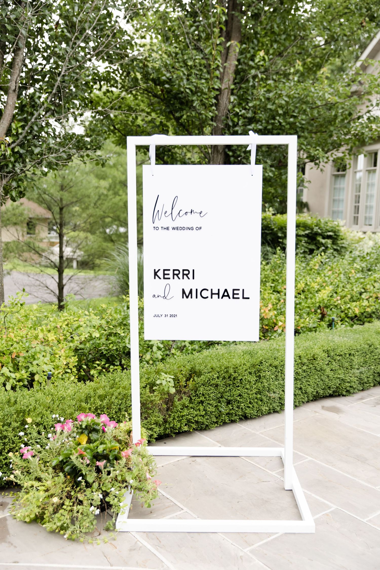 Modern minimalist wedding welcome sign with white frame displaying names on garden pathway.