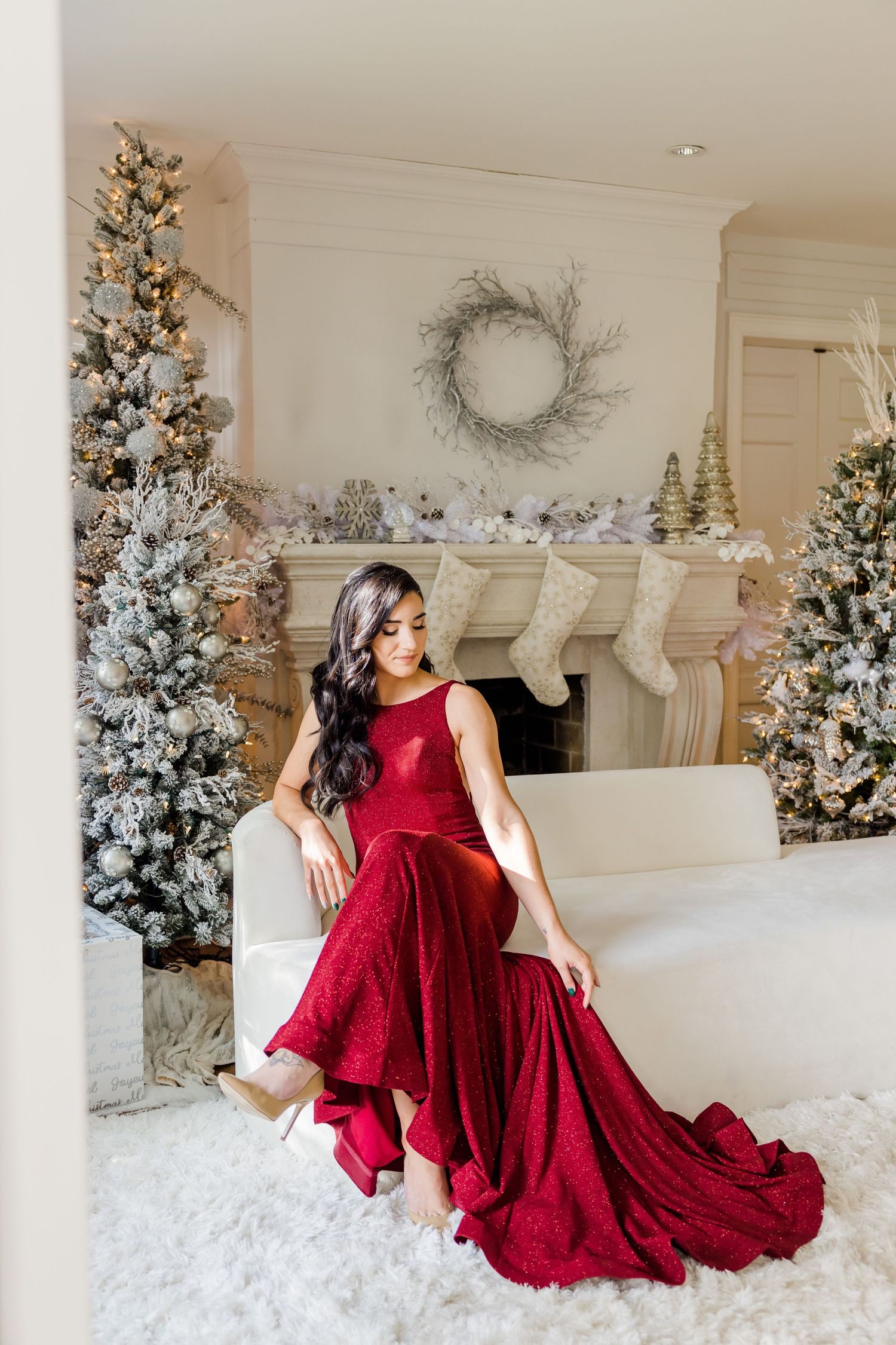 Elegant holiday portrait of woman in red gown seated among decorated Christmas trees.