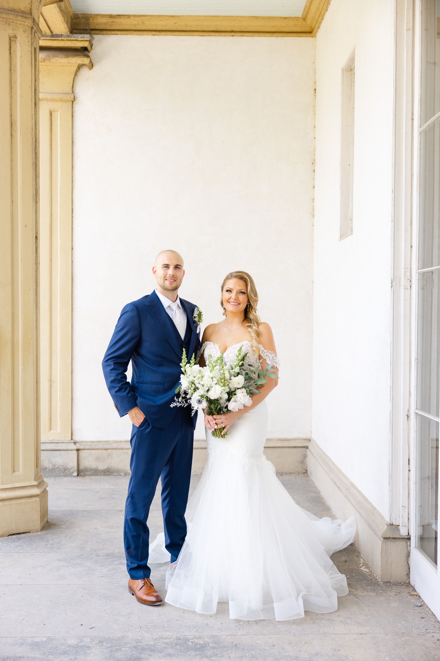 Elegant wedding portrait with navy suit and white dress against classic architecture.