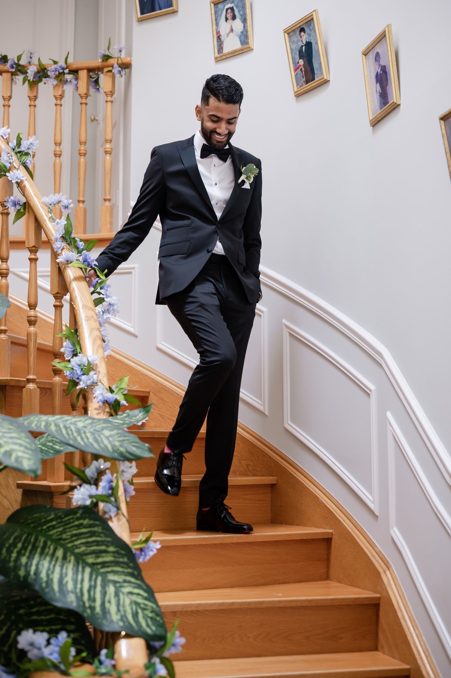 Groom descends decorated staircase adorned with floral arrangements and candles.
