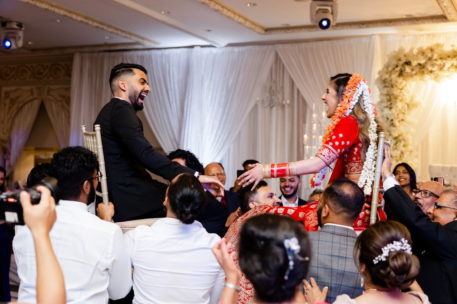 Reception guests lift the couple on chairs during energetic wedding celebration.