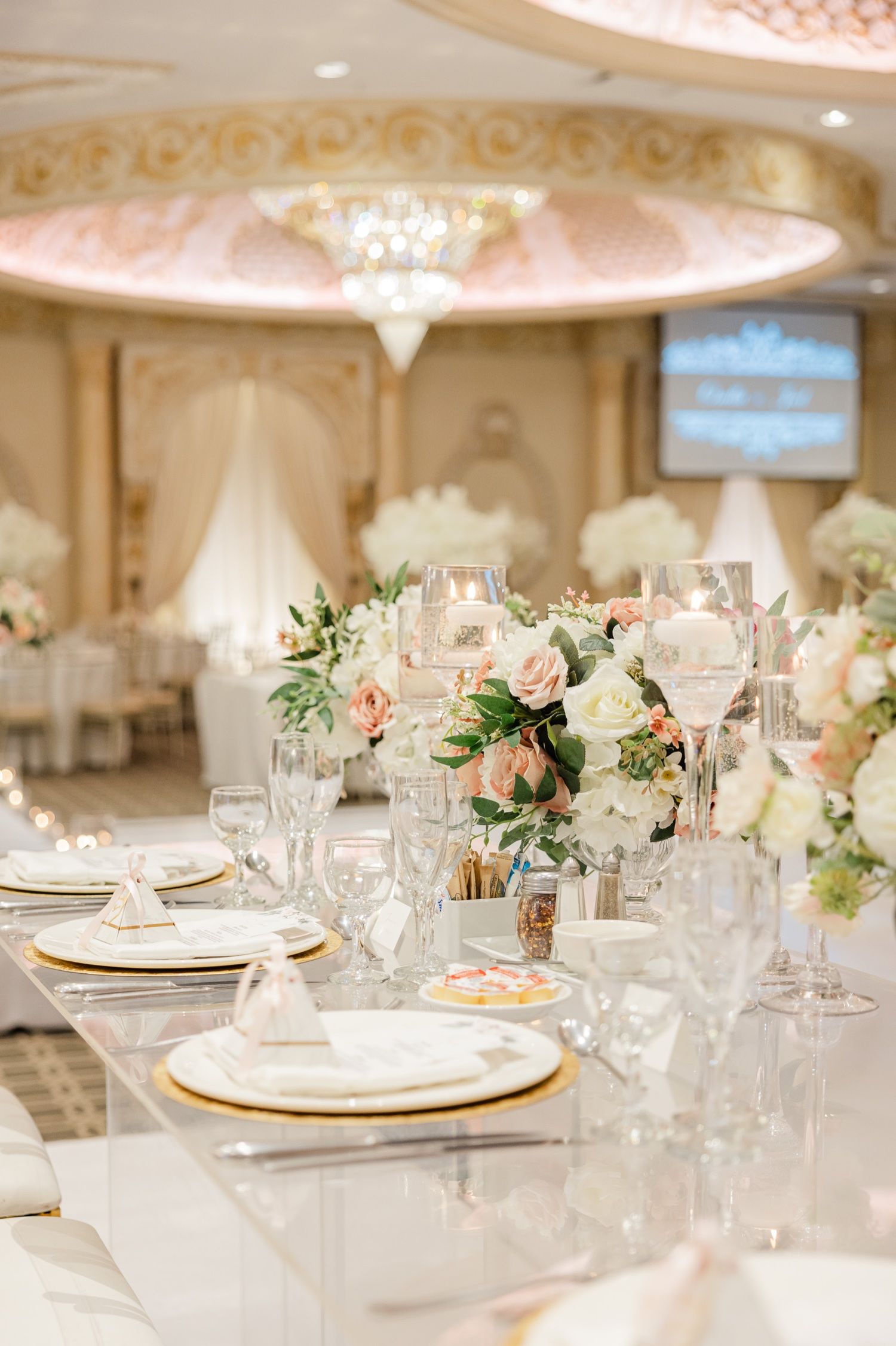 Elegant table setting with pink and white floral centerpieces, gold chargers, and crystal glassware.
