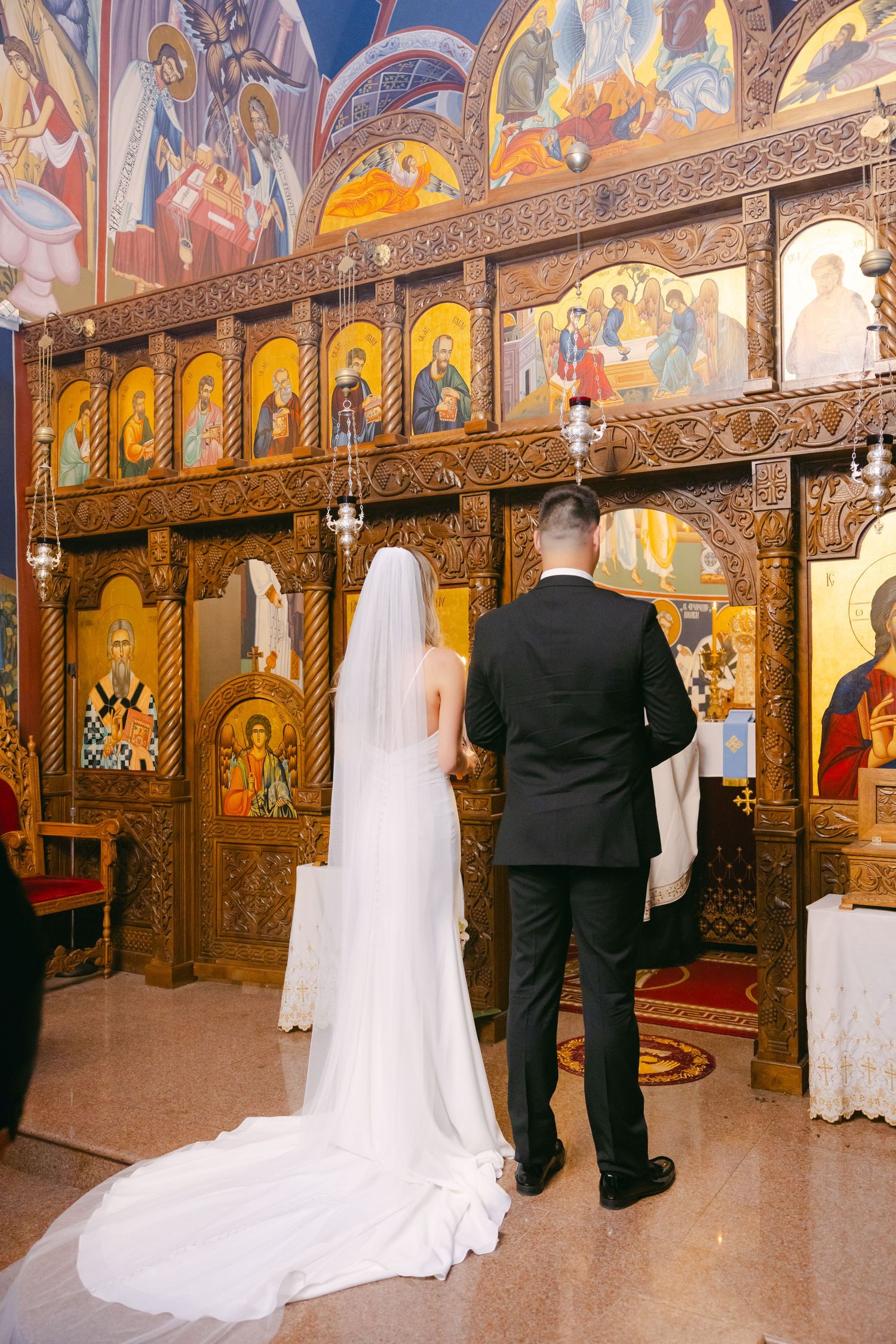 Wedding couple standing before an ornate Orthodox iconostasis with beautiful religious artwork.