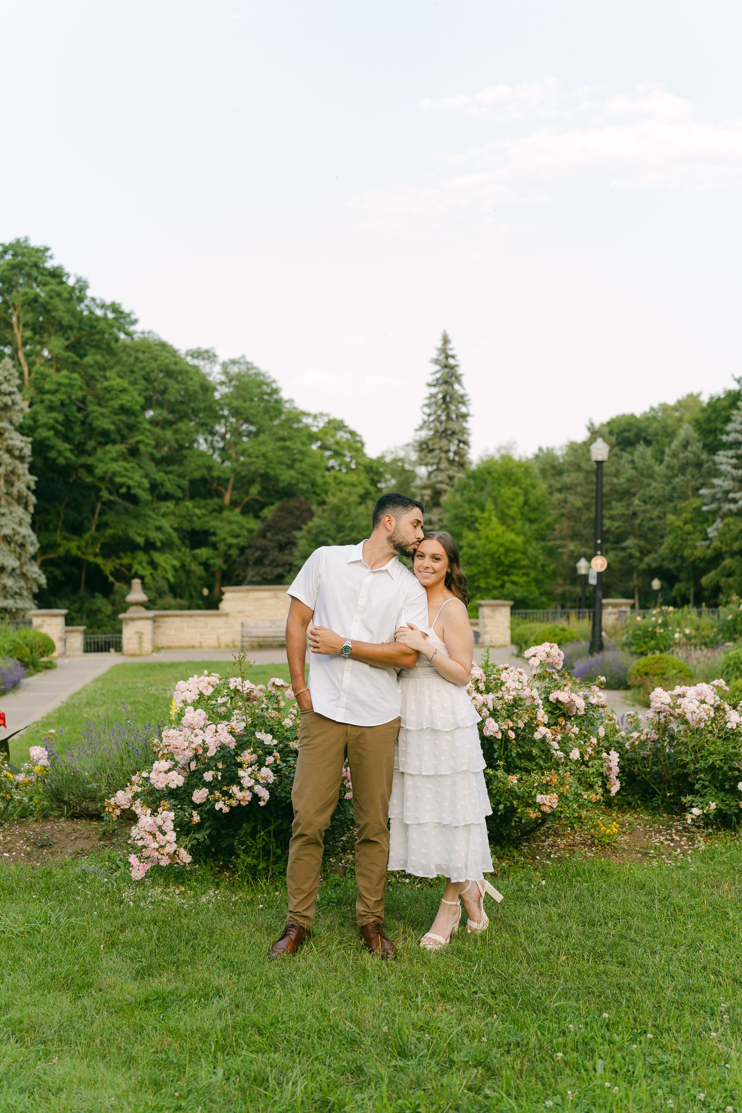 A couple poses together in a beautiful garden setting with pink roses and lush greenery.