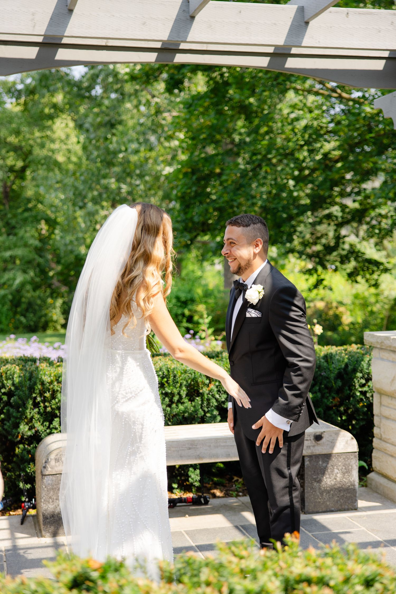 Wedding couple shares a special moment under a pergola surrounded by manicured gardens.