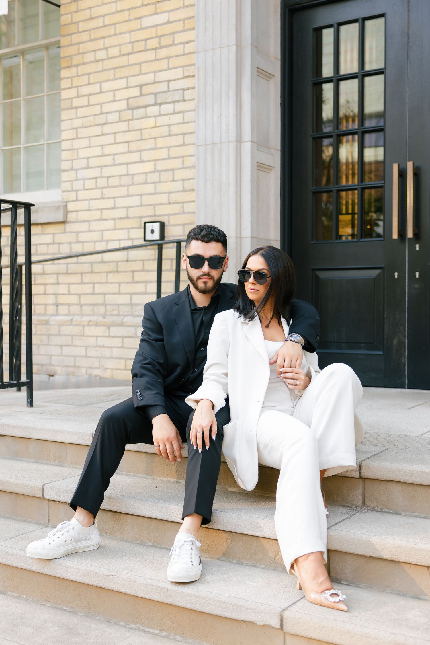 Trendy couple in coordinated formal wear poses on steps of luxury boutique.