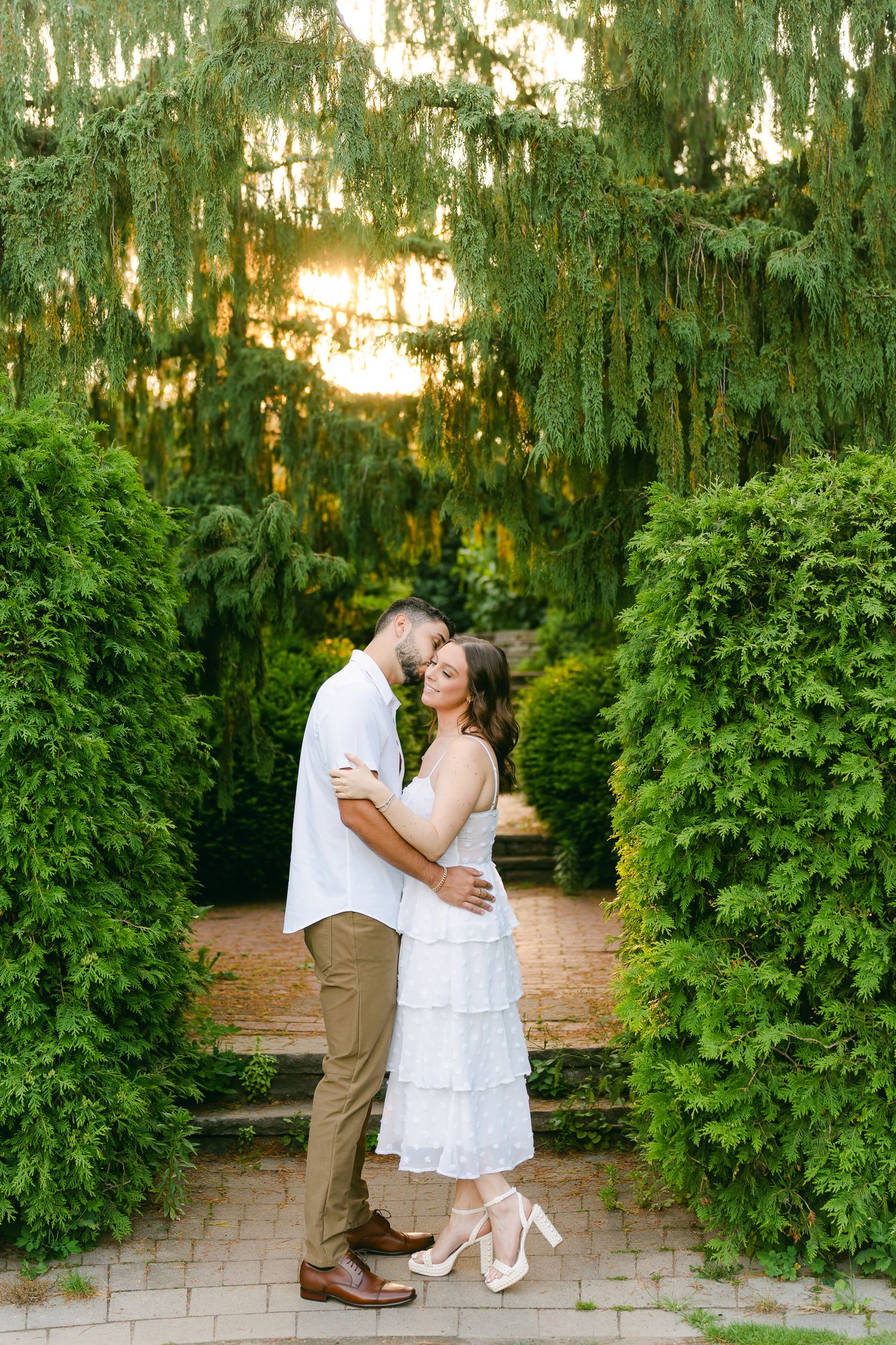 Joyful couple dancing on garden steps surrounded by manicured hedges and weeping willows.