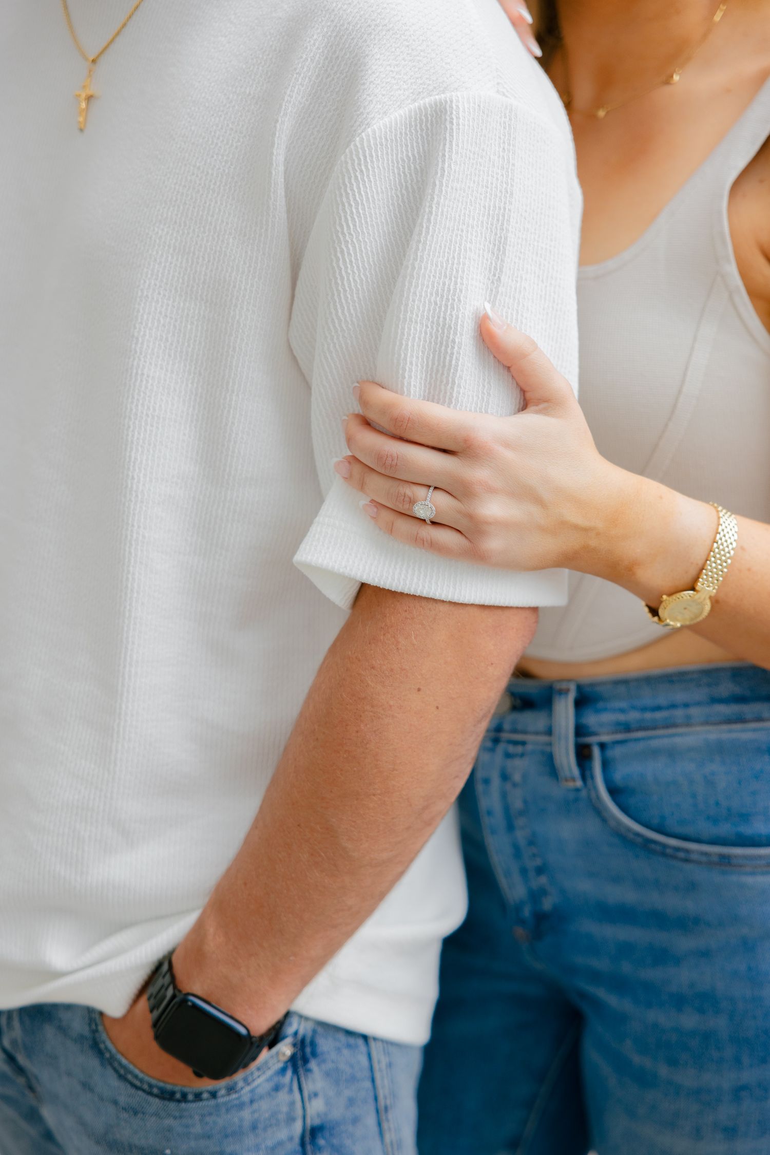 Close-up shot of couple holding hands, wearing white sweater and jewelry with blue jeans.