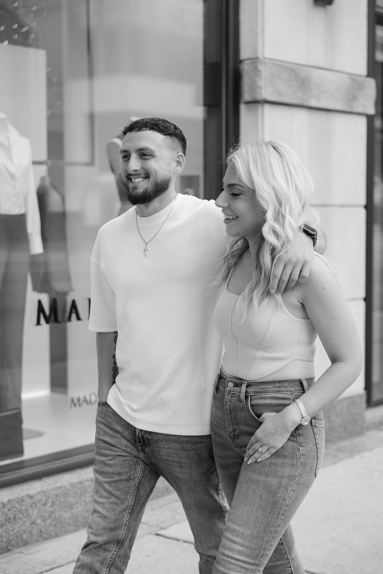 Black and white portrait of happy couple in casual attire outside store.