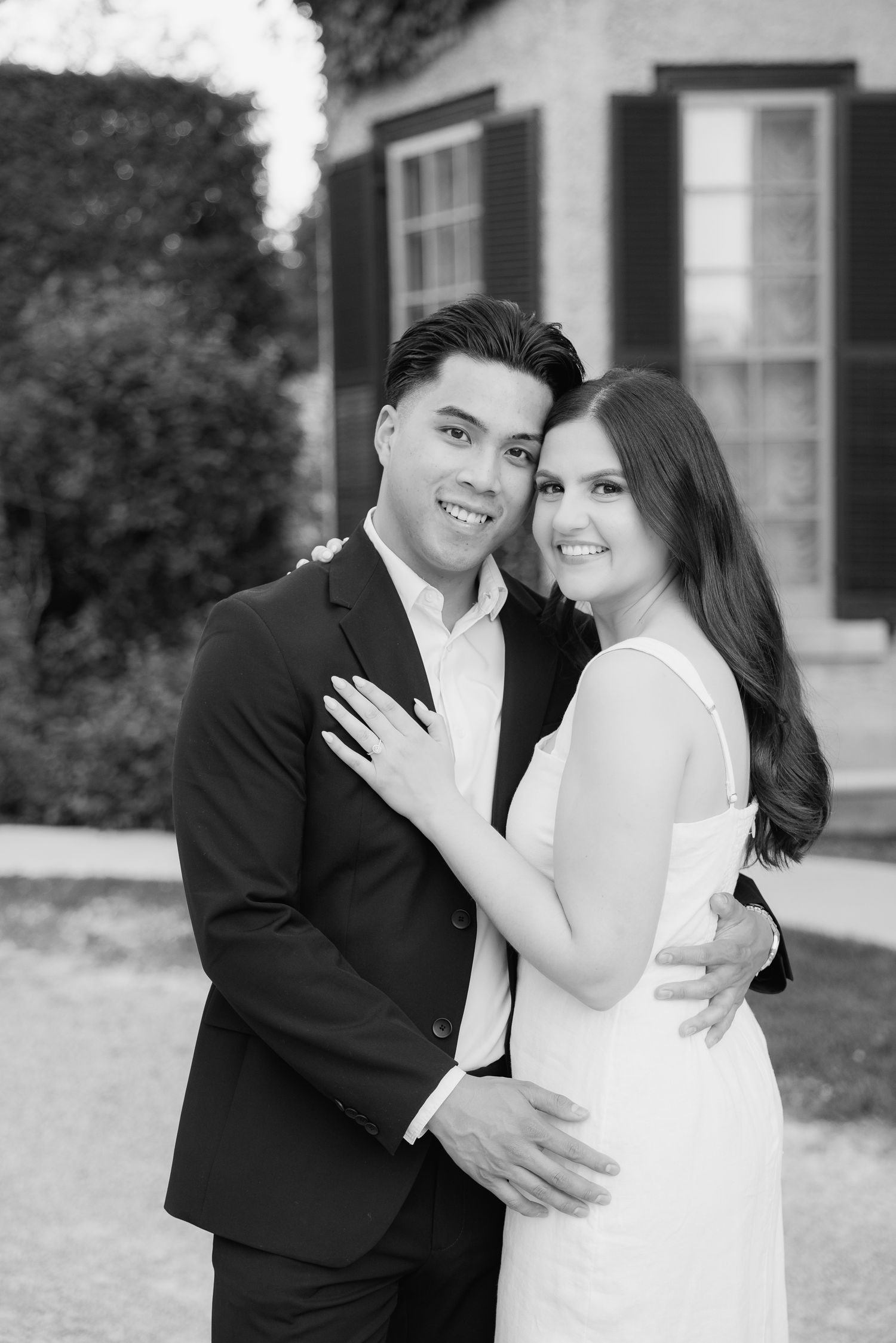 Black and white portrait of couple in formal wear by mansion windows.