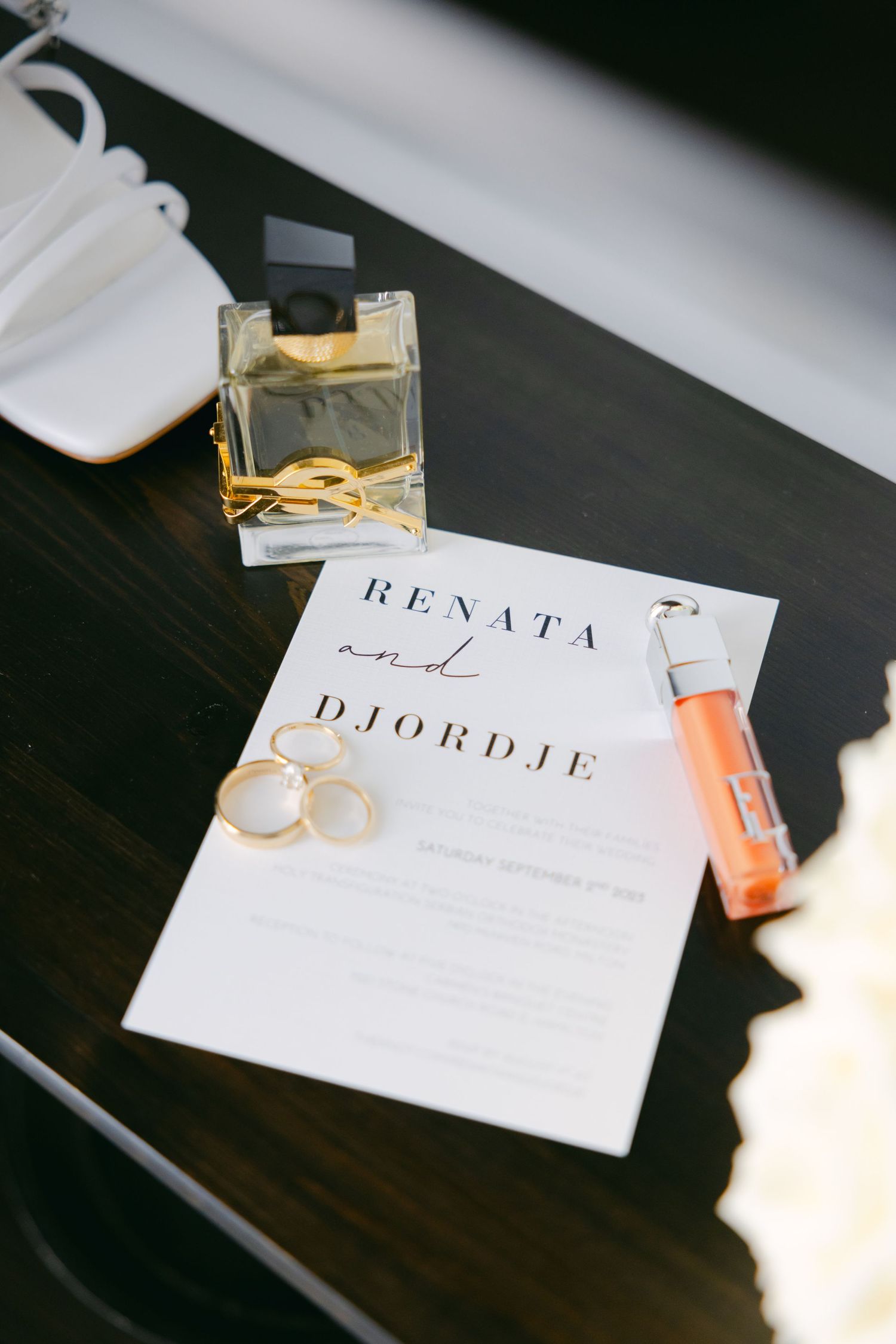 Wedding invitation for Renata and Djordje with perfume bottle, rings and details on dark wooden surface.
