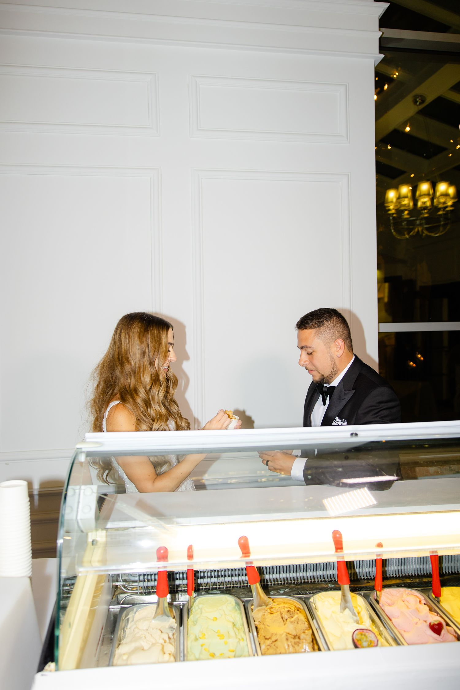 Couple enjoying gelato selections at an elegant indoor reception with chandeliers.
