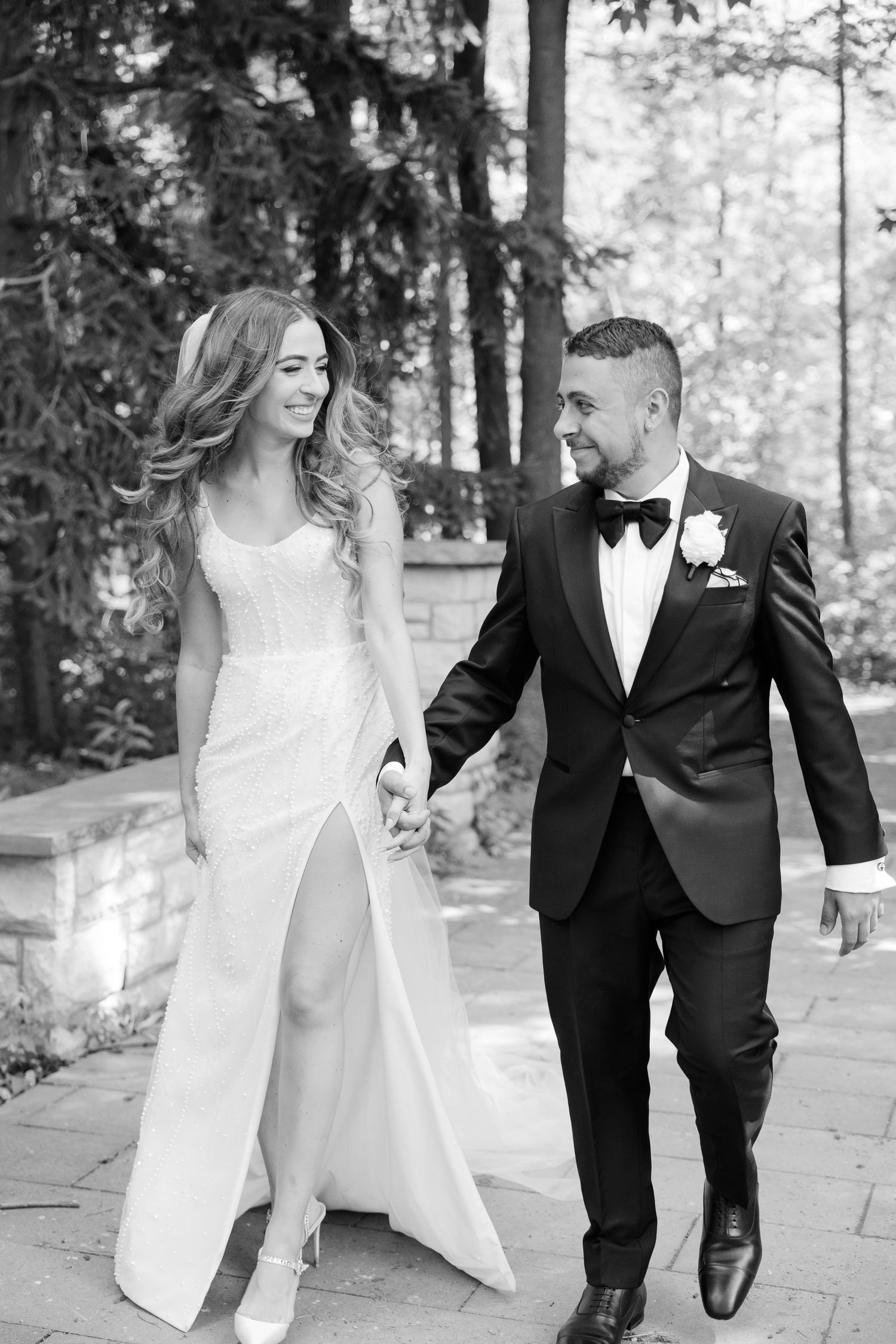 Black and white portrait of newlyweds walking together on garden path.