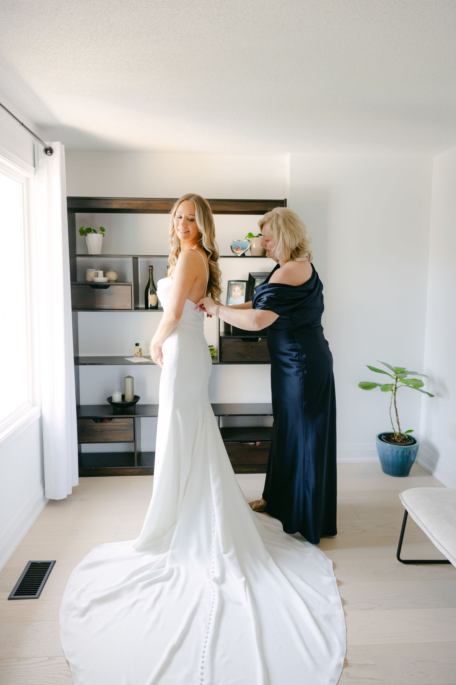 A wedding dress being fitted in a minimalist room with dark wooden shelving.