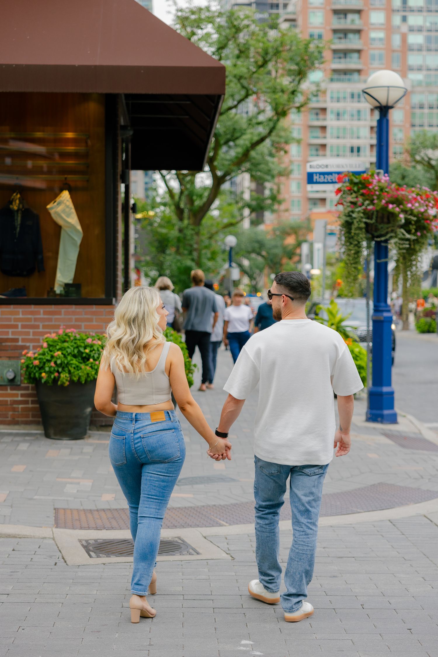 Couple walking hand in hand past retail stores in a downtown area.