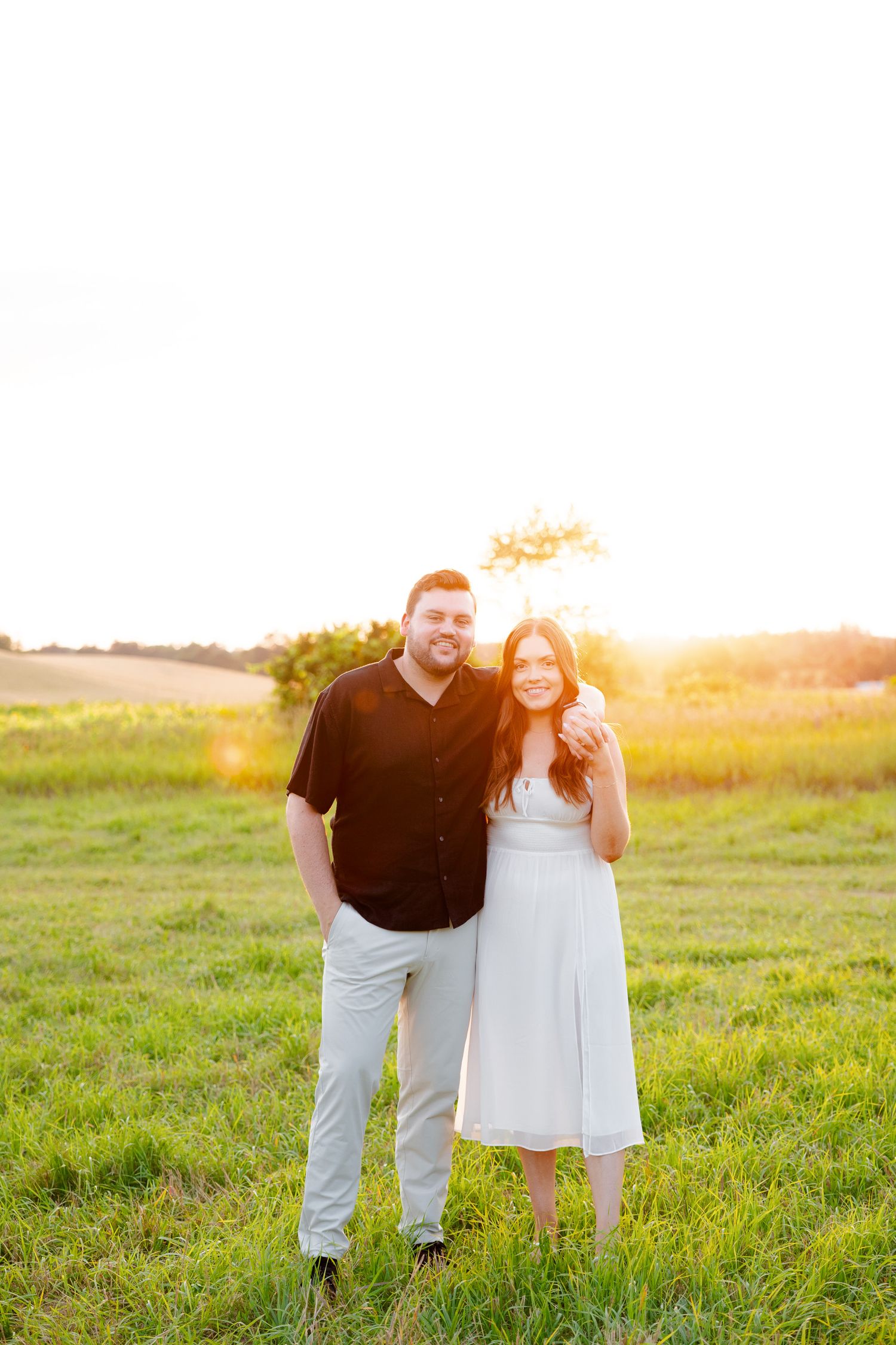 Happy couple poses together in sunlit field during summer engagement session.