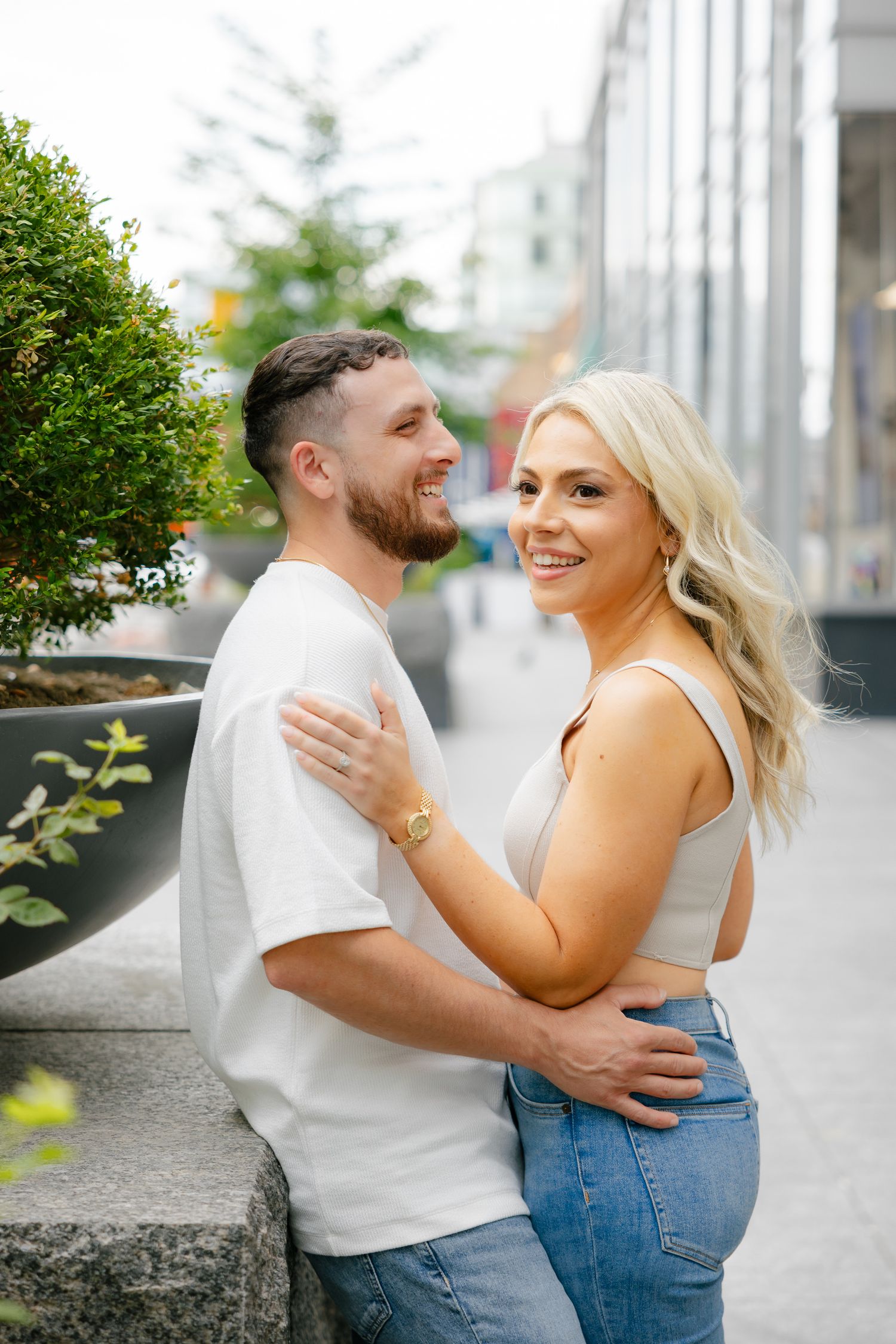 A couple embracing outdoors near decorative planters and a modern building facade.