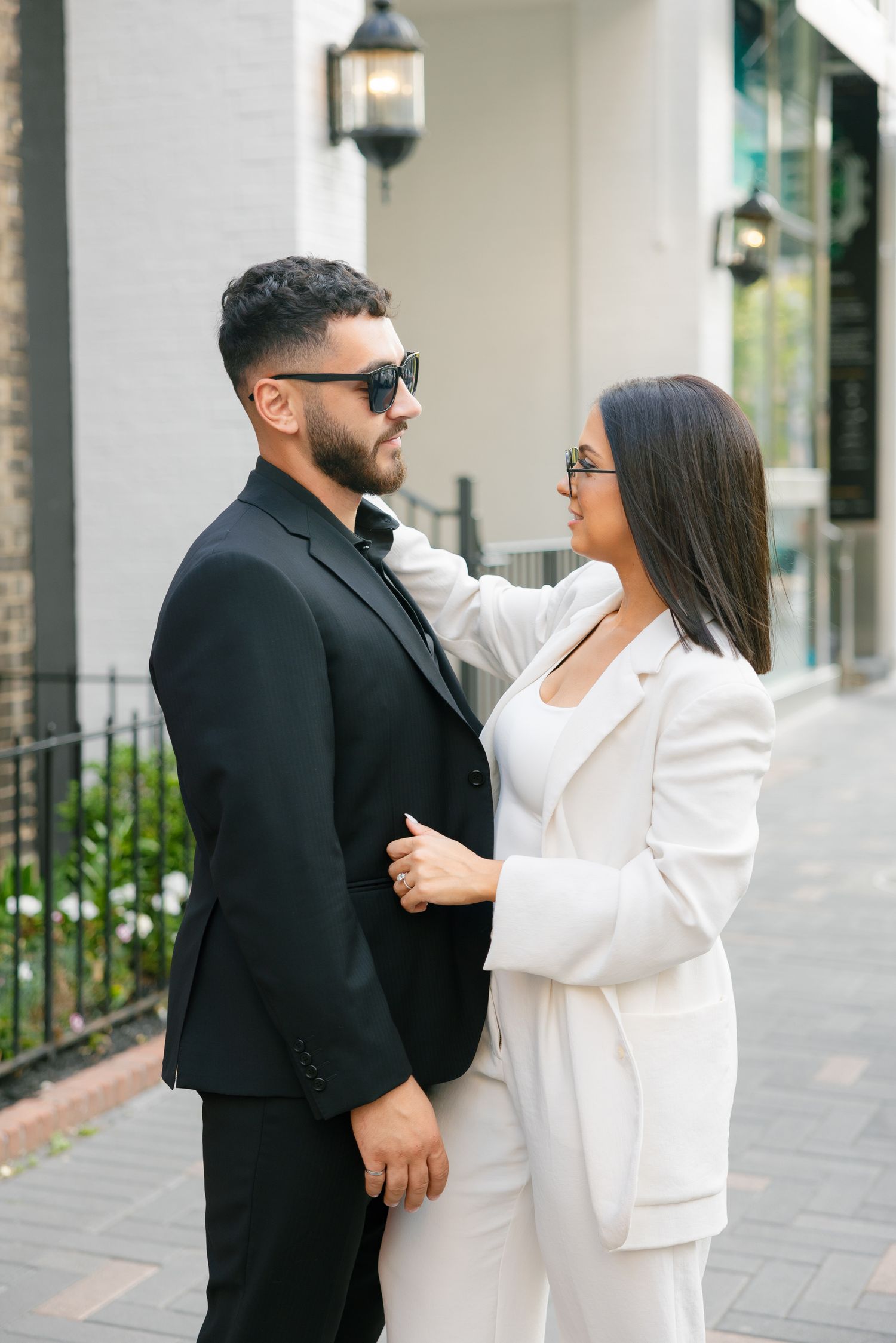A couple shares an intimate moment on a city sidewalk while wearing coordinated formal attire.