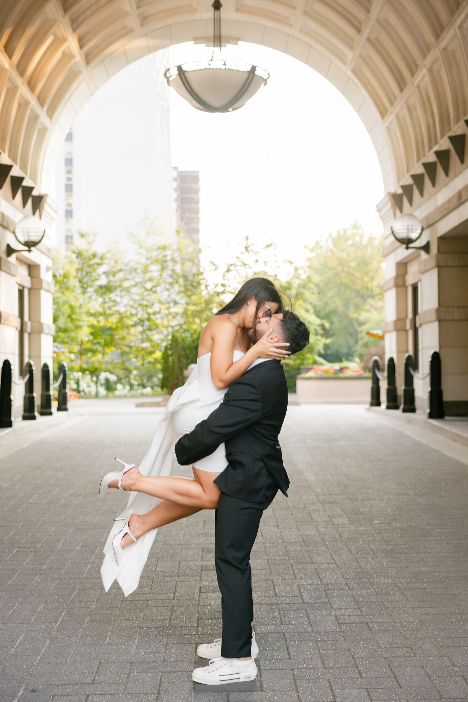 Sunny romantic portrait of a couple in wedding attire embracing under an elegant archway.