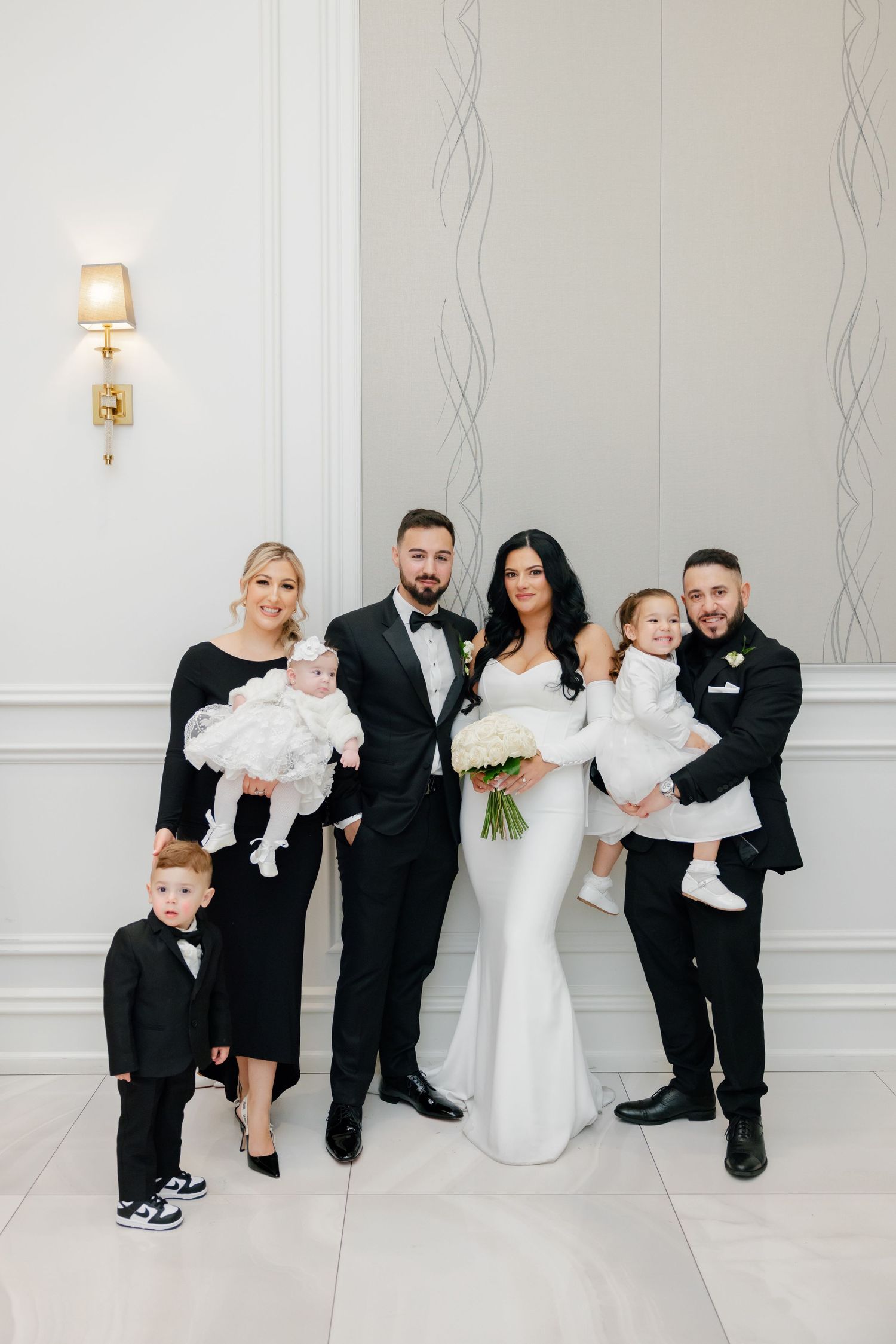 Wedding party photo with children in formal attire against elegant white interior.