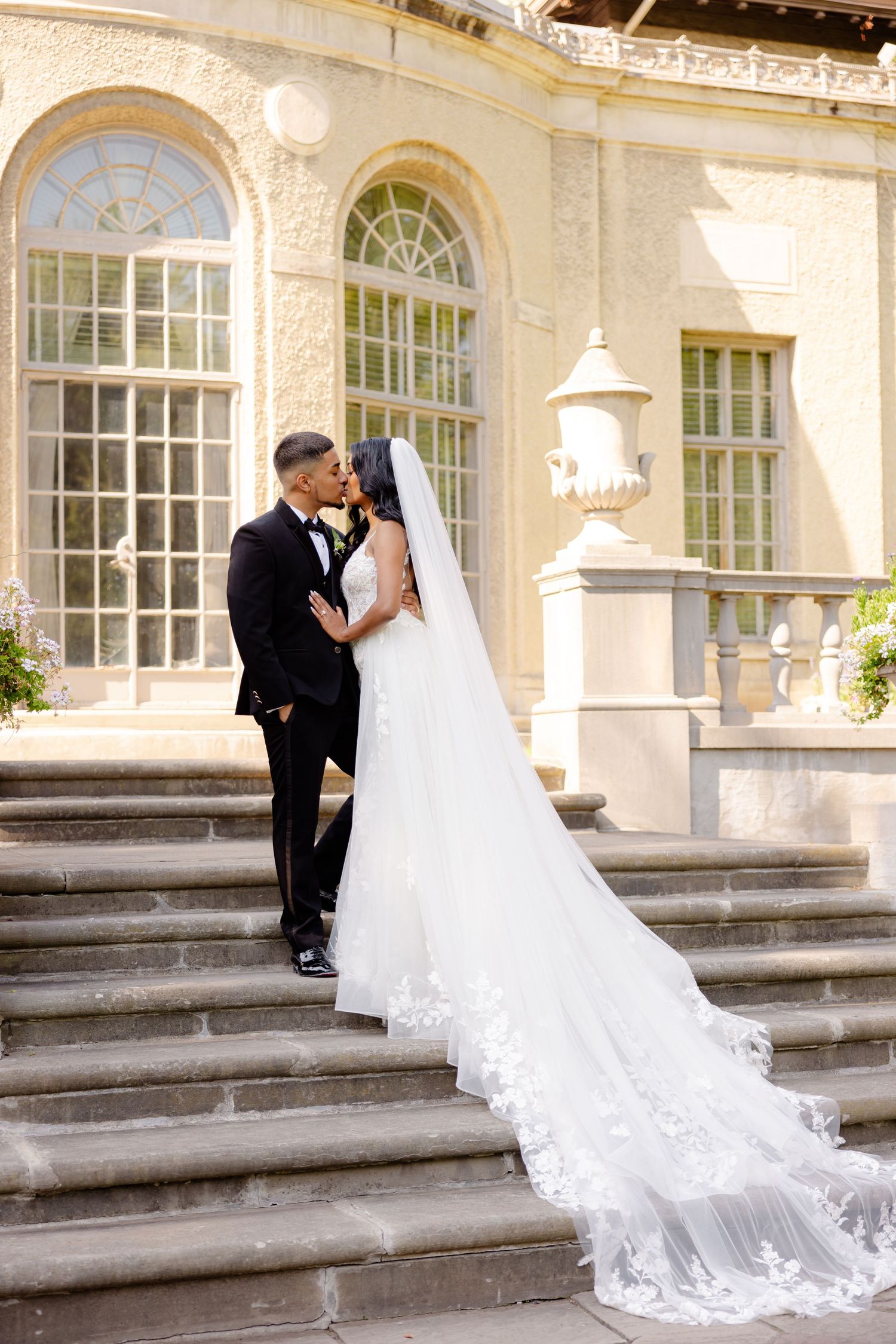 A romantic wedding portrait on stone steps with a flowing cathedral veil and historic architecture.