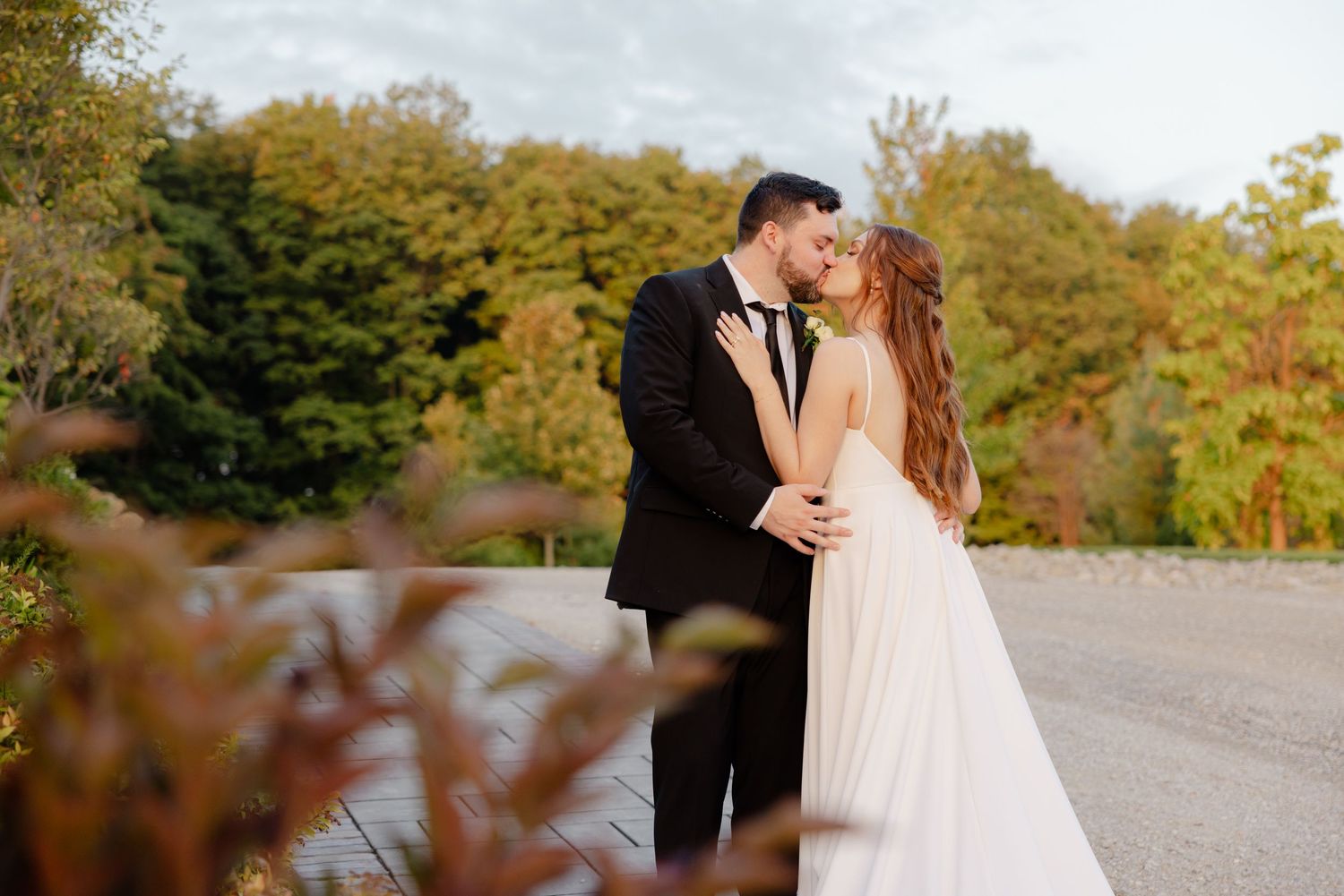Romantic wedding moment captured outdoors with stone pathway and golden autumn trees.