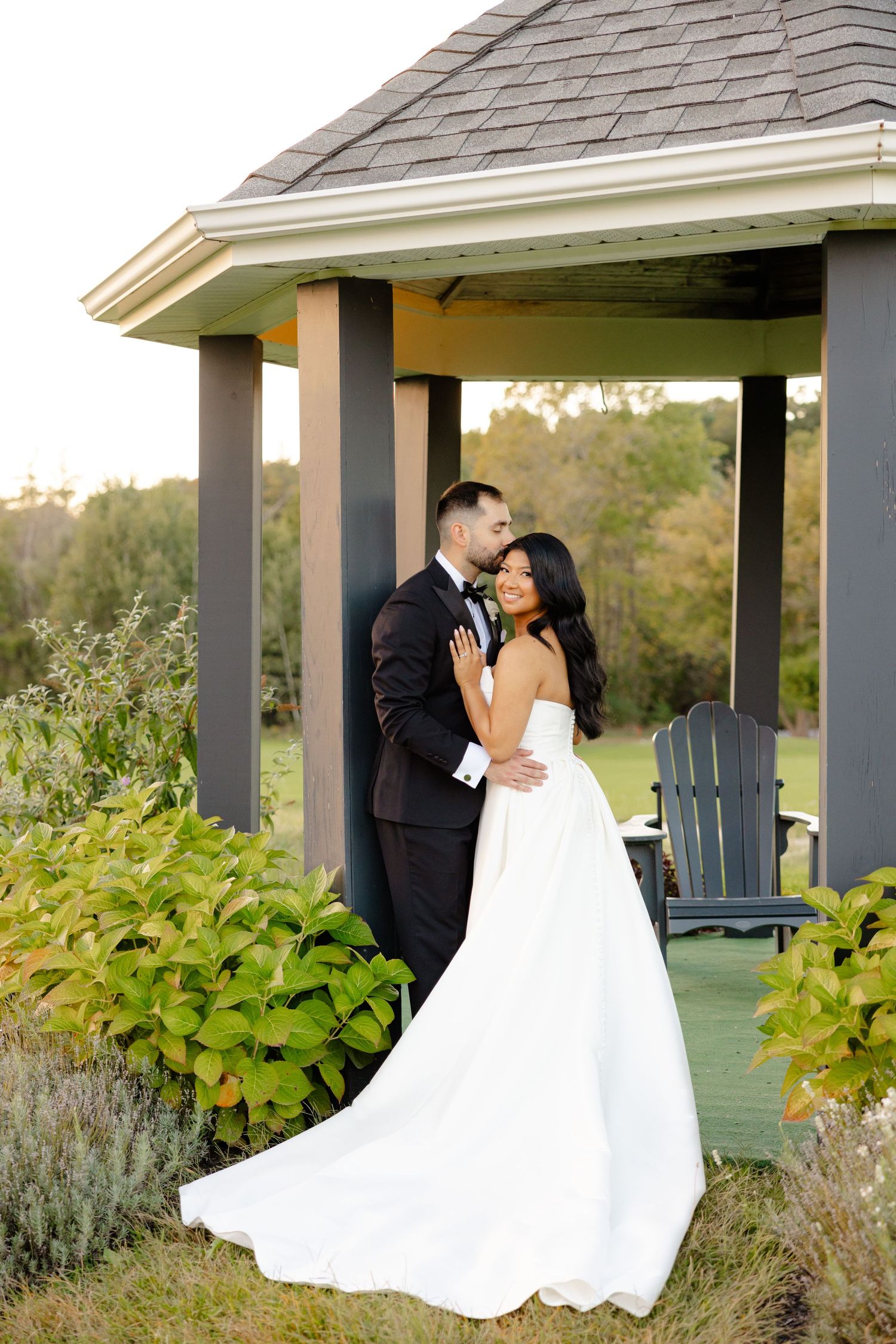 A romantic wedding portrait captured in a garden gazebo with lush summer foliage.