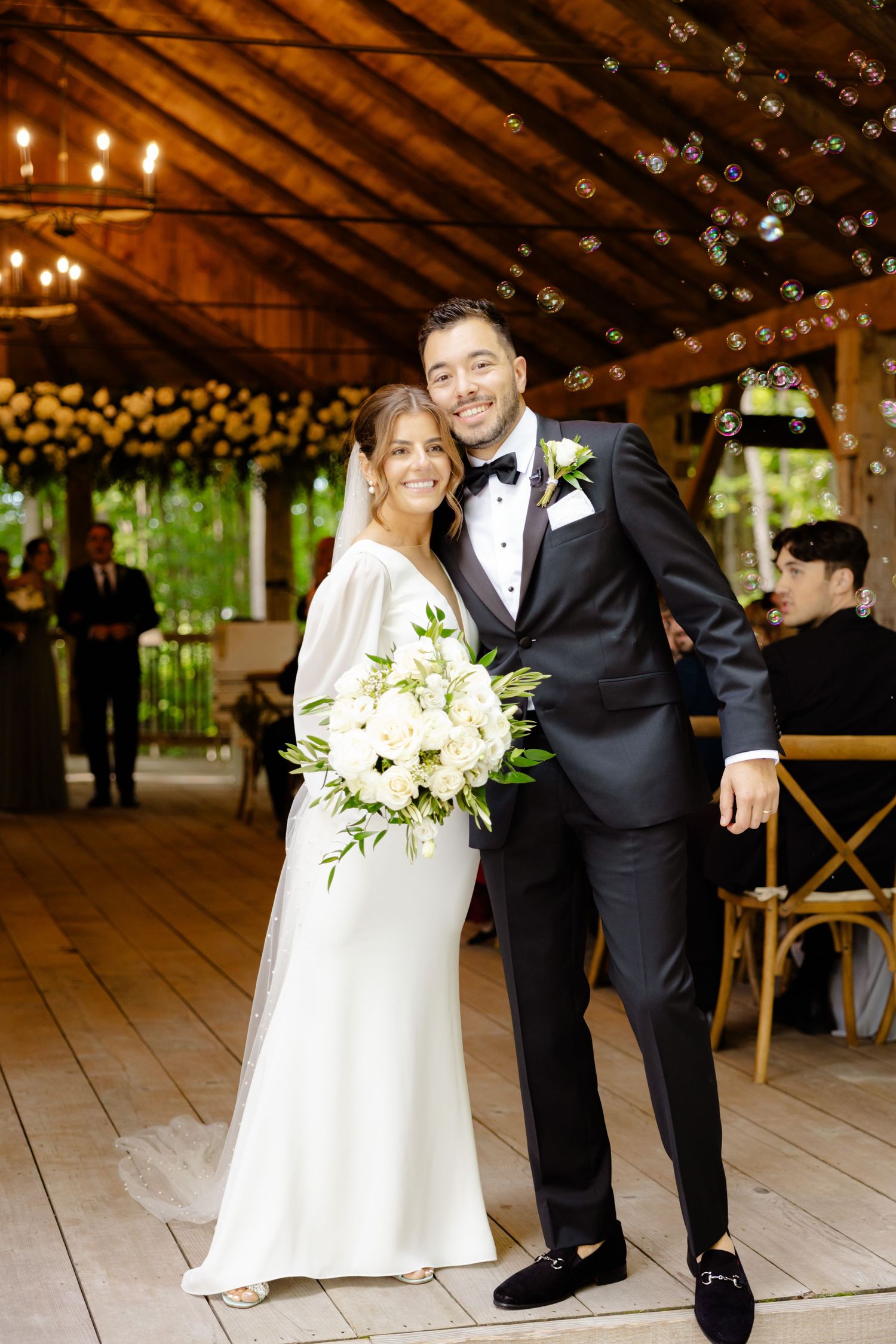 Wedding portrait in a warmly lit wooden pavilion with floral decorations and rustic charm.