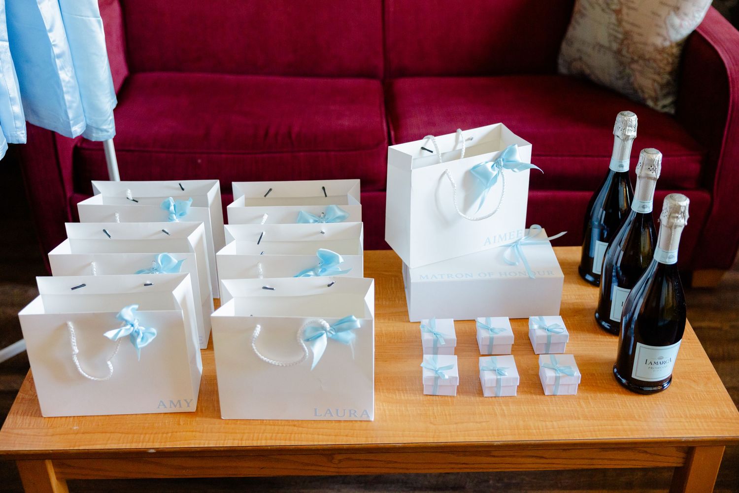 Wedding favors and champagne bottles arranged on wooden table with white gift bags.