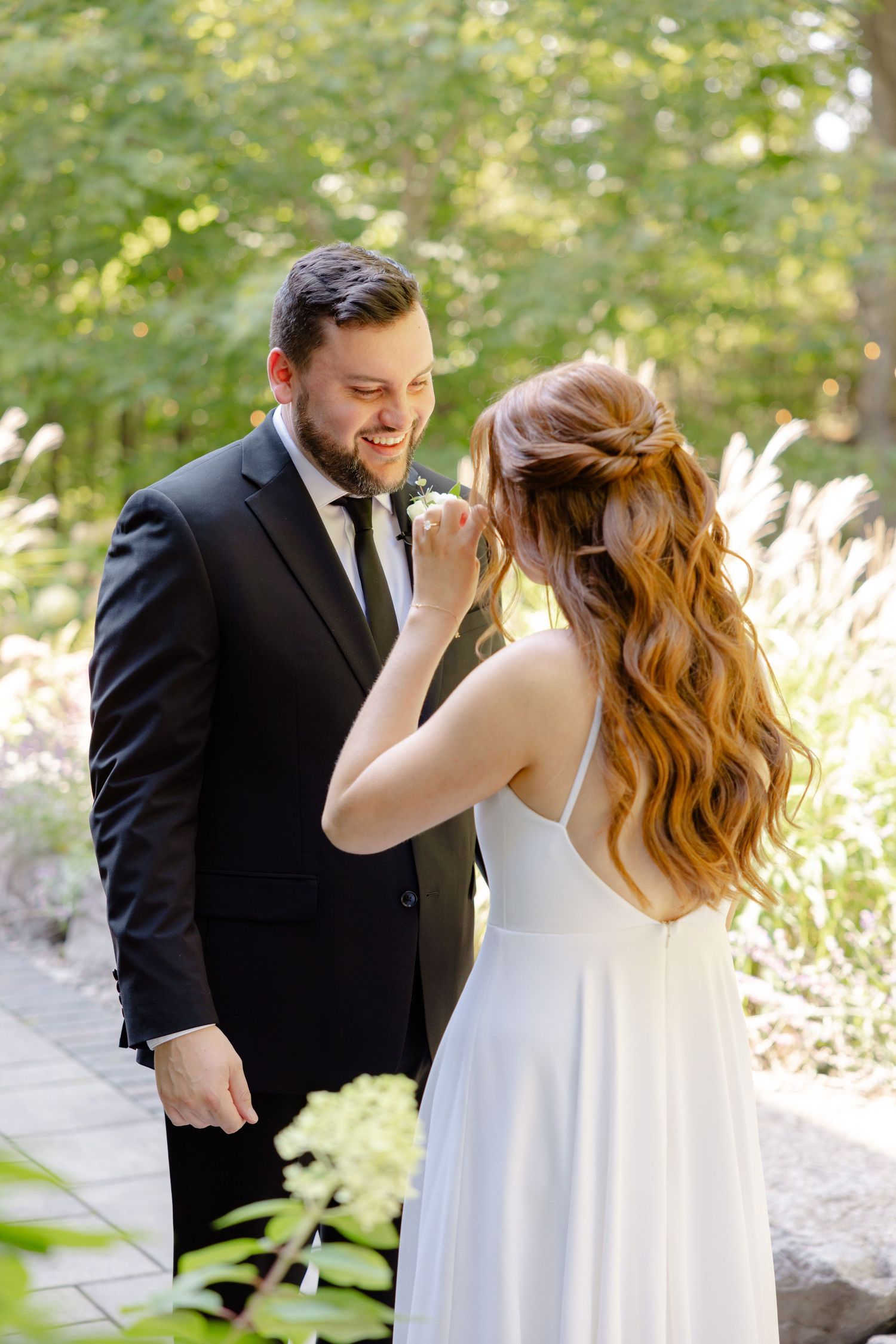 A candid wedding moment captured in a sunlit garden setting with natural landscaping.