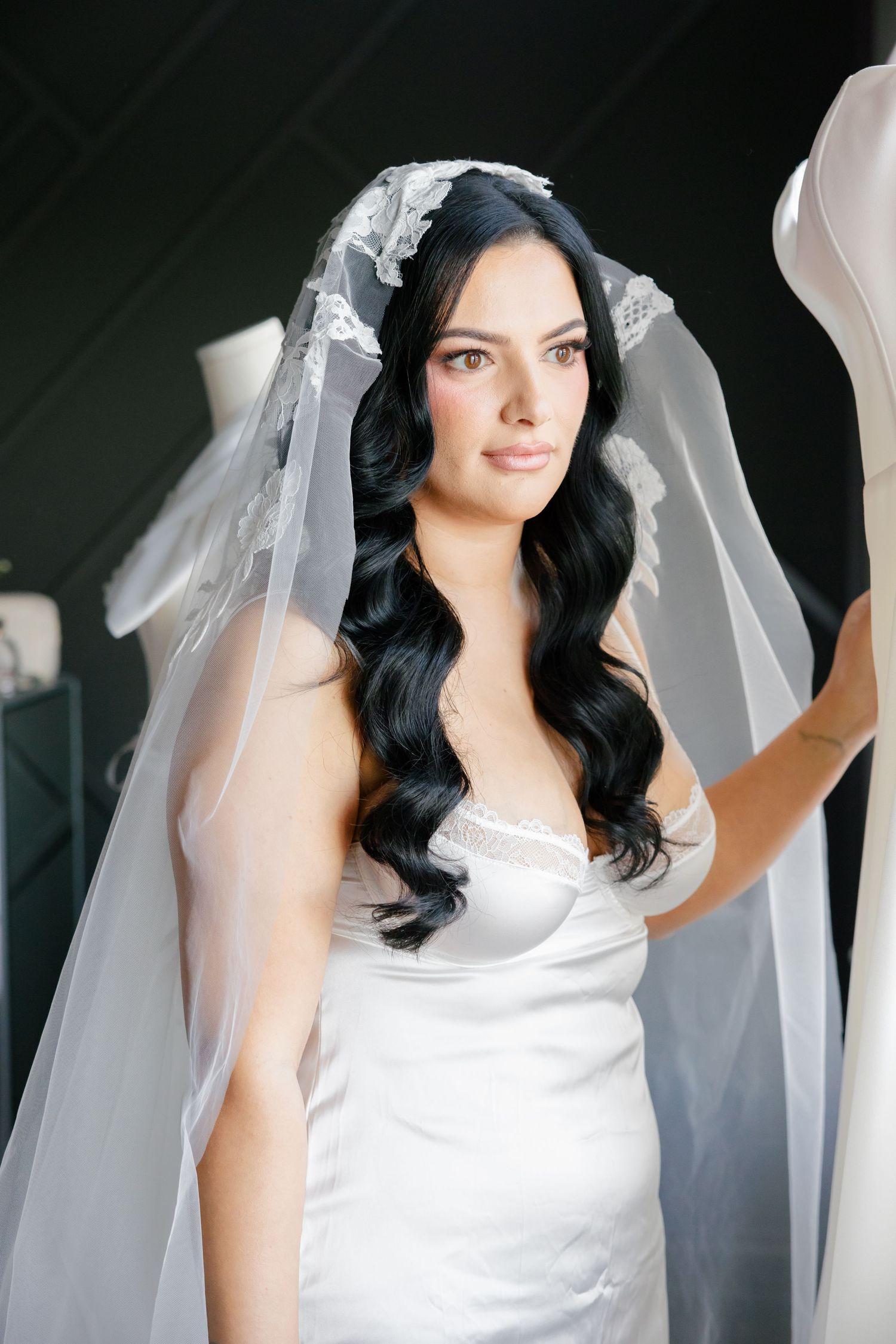 Elegant bridal portrait showing a flowing white dress and long dark wavy hair beneath a sheer veil.