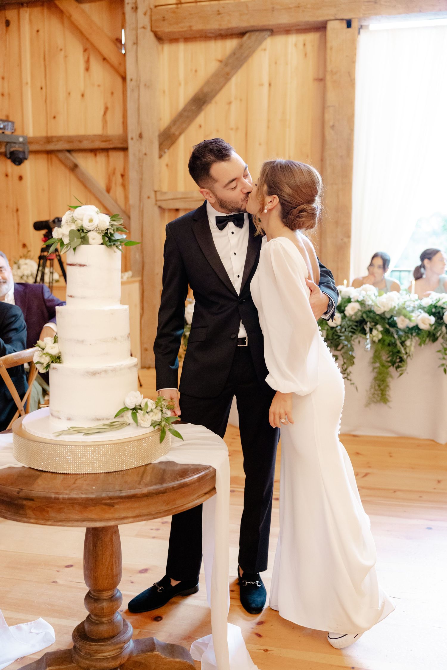 A tender moment between newlyweds next to their wedding cake in a rustic barn setting.